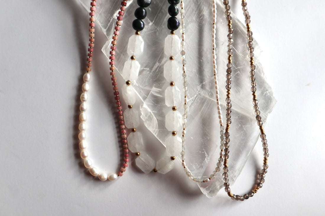 Handmade gemstone necklaces for Mother's Day laid flat on a white selenite slab, featuring freshwater pearl, rhodonite, moonstone, and smoky quartz designs by Auréad Designs