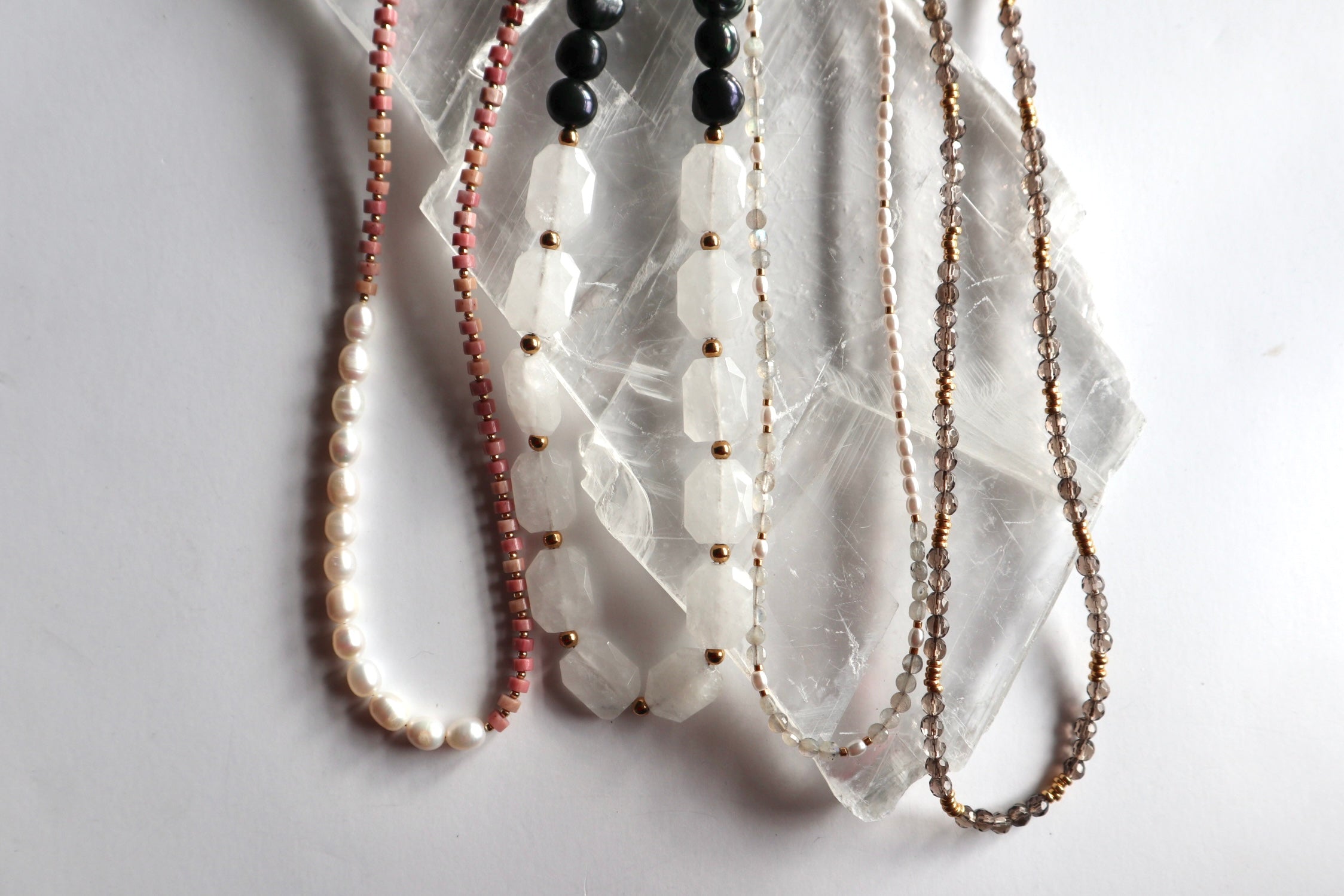 Handmade gemstone necklaces for Mother's Day laid flat on a white selenite slab, featuring freshwater pearl, rhodonite, moonstone, and smoky quartz designs by Auréad Designs