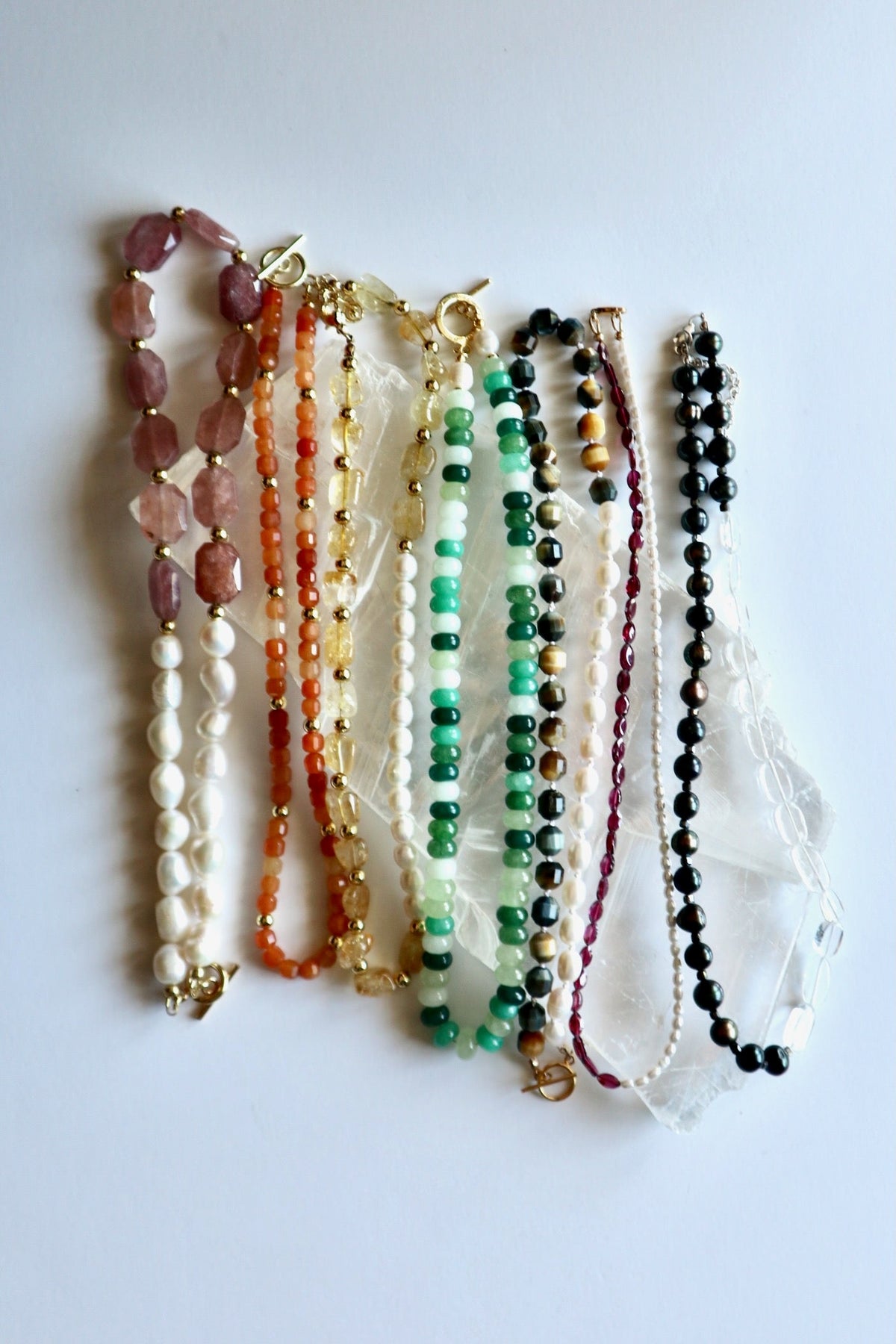 Multi-stone gemstone necklace collection by Auréad Designs displayed on selenite slab, showing color variety across the collection