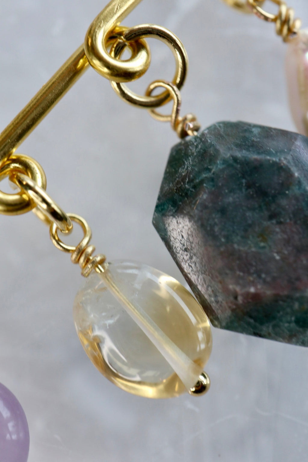 Close-up detail of the Amorine brooch by Auréád Designs, showing a pale yellow citrine oval and dark teal apatite charm hanging from the gold stainless steel pin clasp