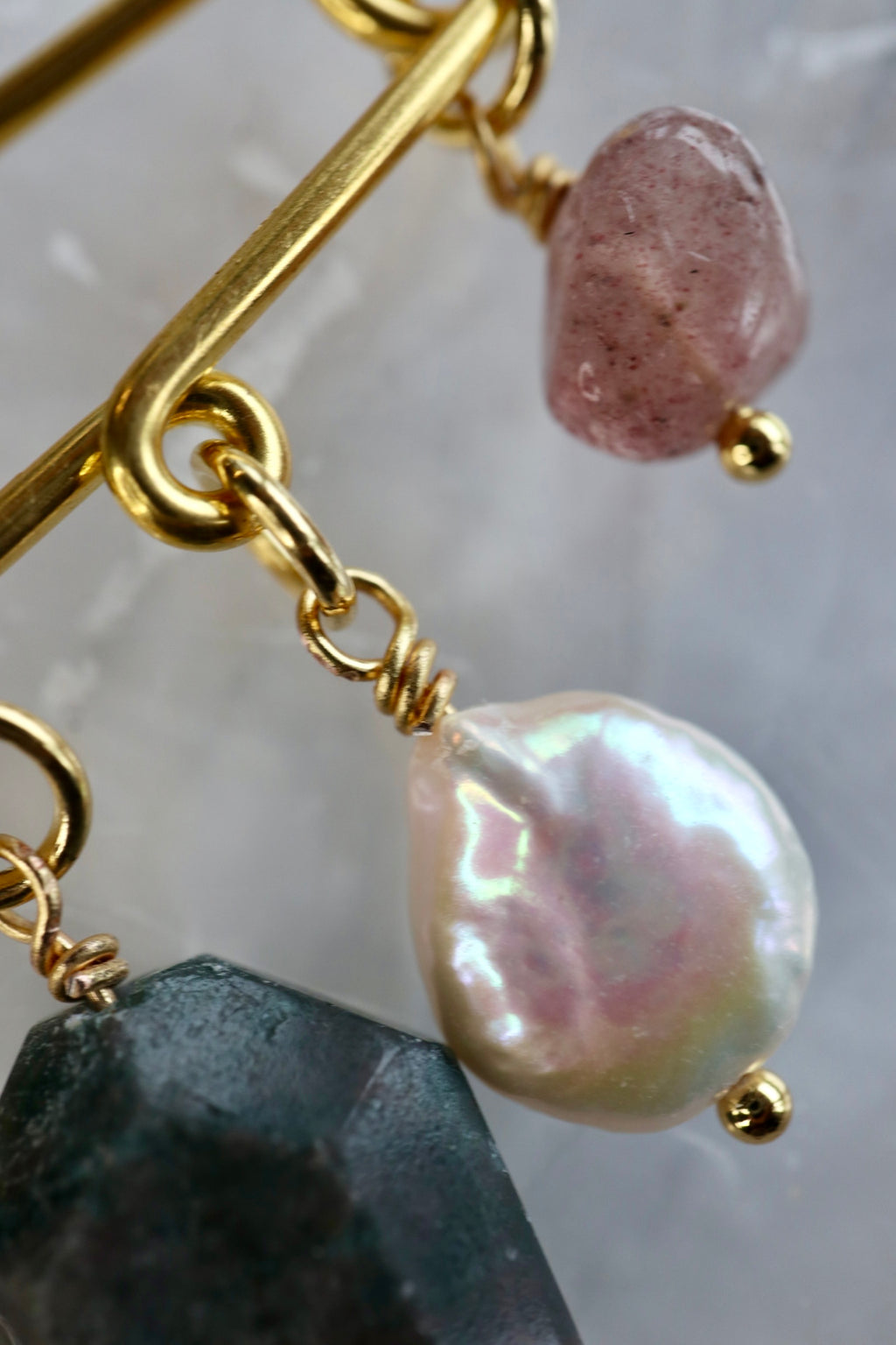 Close-up detail of the Amorine brooch by Auréád Designs, showing an iridescent freshwater coin pearl and rough strawberry quartz charm hanging from a gold stainless steel pin