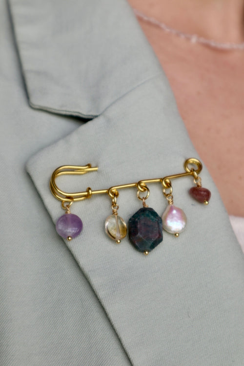 Amorine mixed gemstone brooch by Auréád Designs pinned to the lapel of a sage green blazer, showing amethyst, citrine, apatite, freshwater pearl, and strawberry quartz charm drops against the fabric
