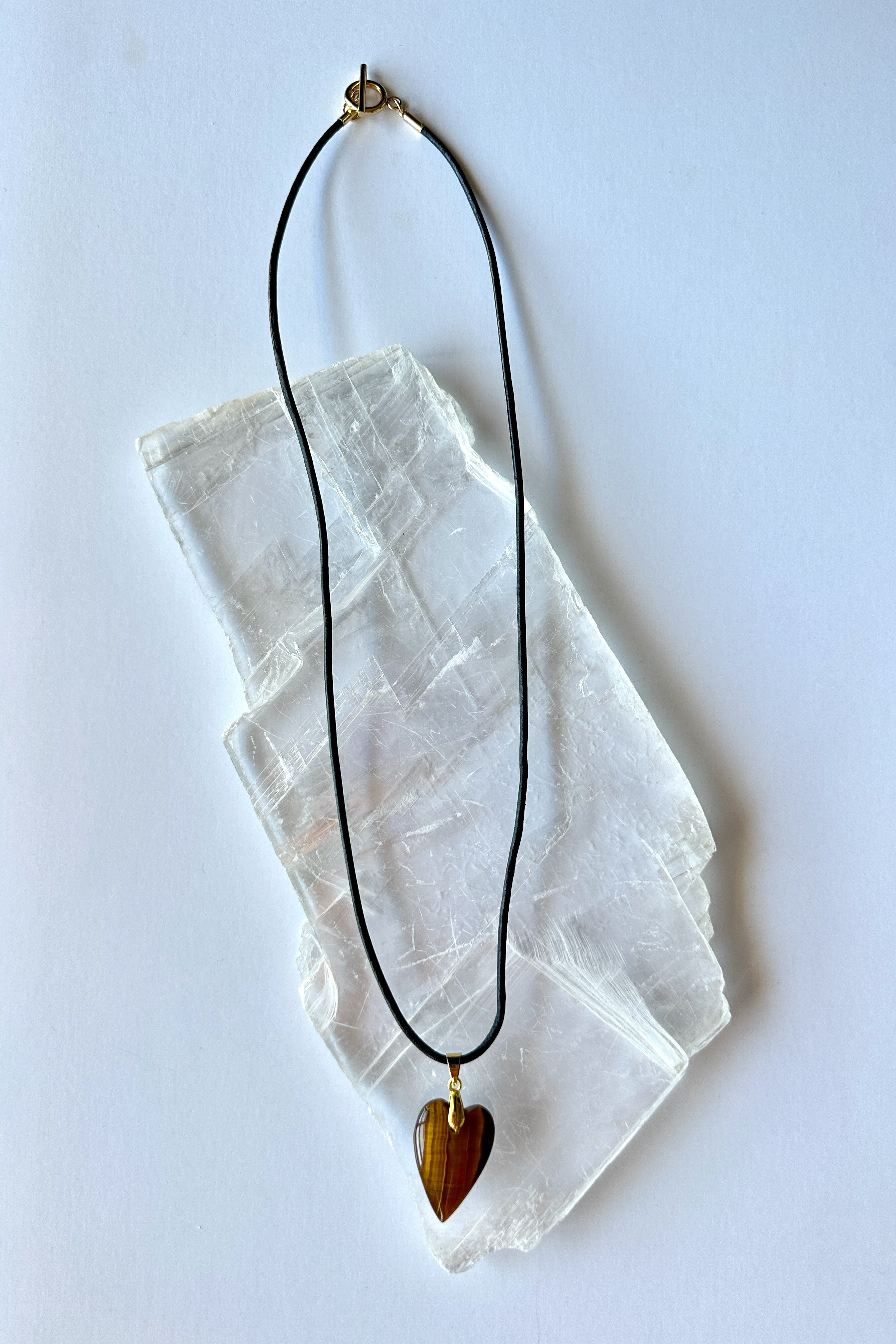 Ardene tiger eye heart pendant necklace by Auréad Designs on selenite slab, close-up showing black leather cord