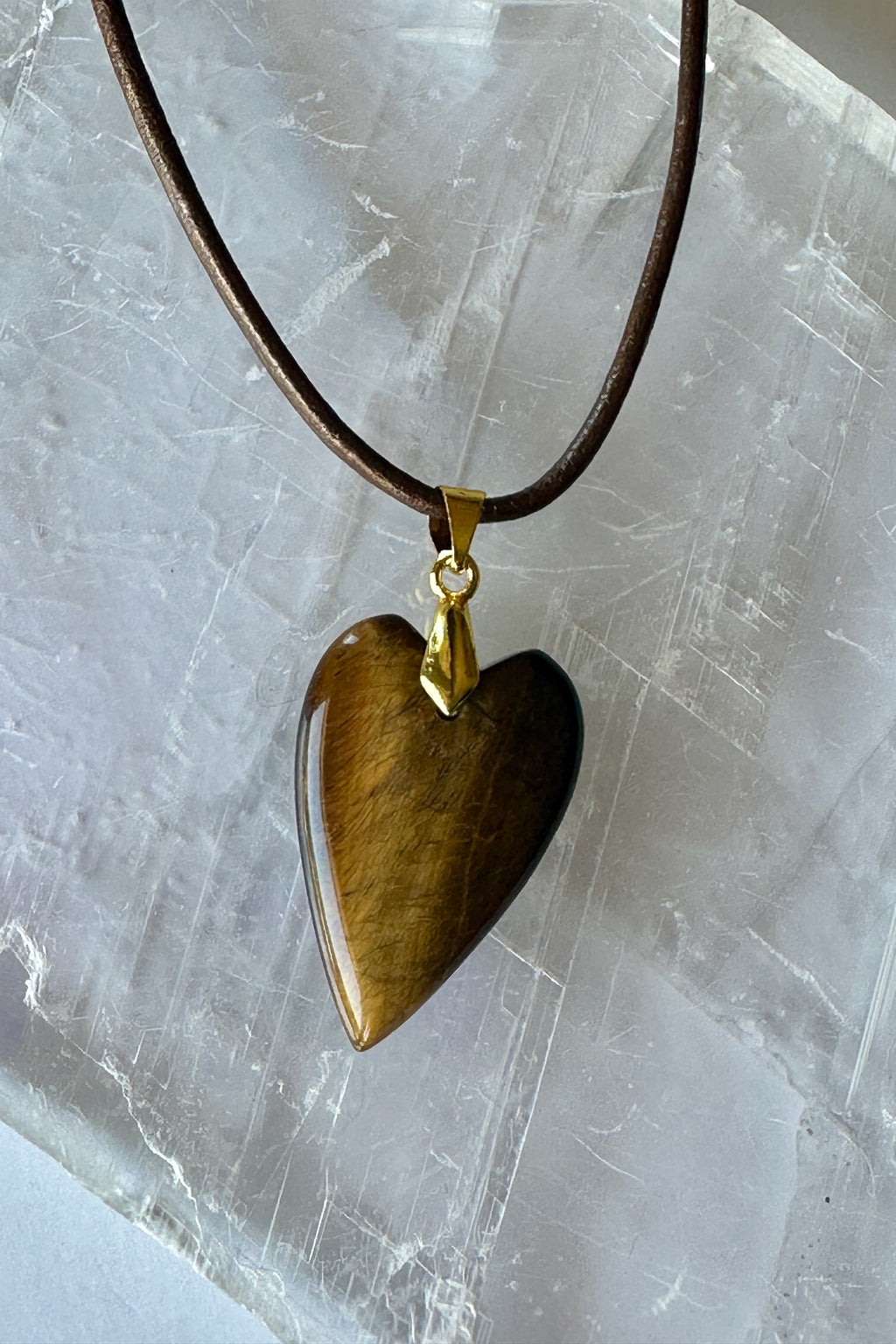 Ardene tiger eye heart pendant necklace by Auréad Designs on selenite slab, close-up showing bronze leather cord