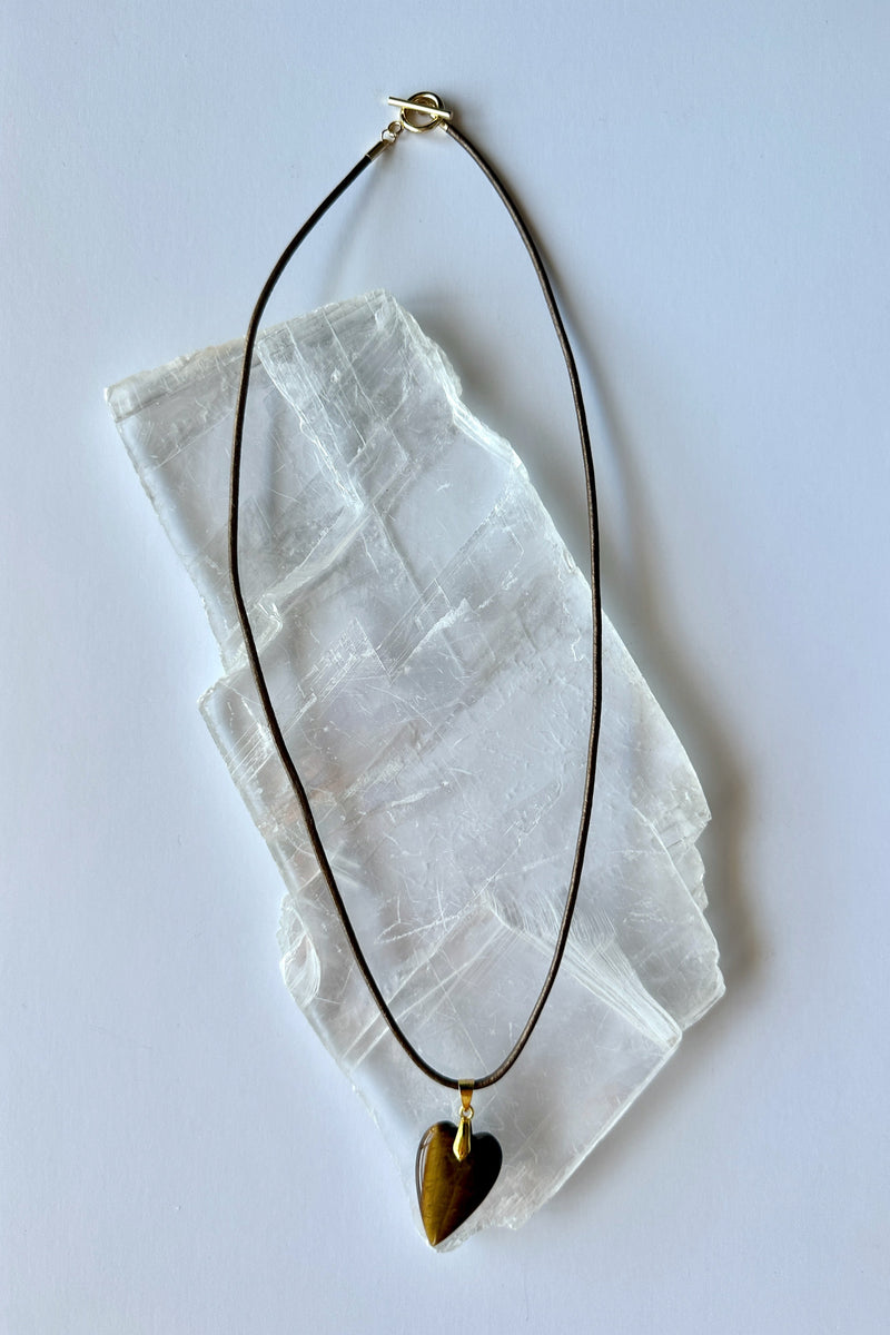 Ardene tiger eye heart pendant necklace by Auréad Designs on white selenite slab, bronze leather cord