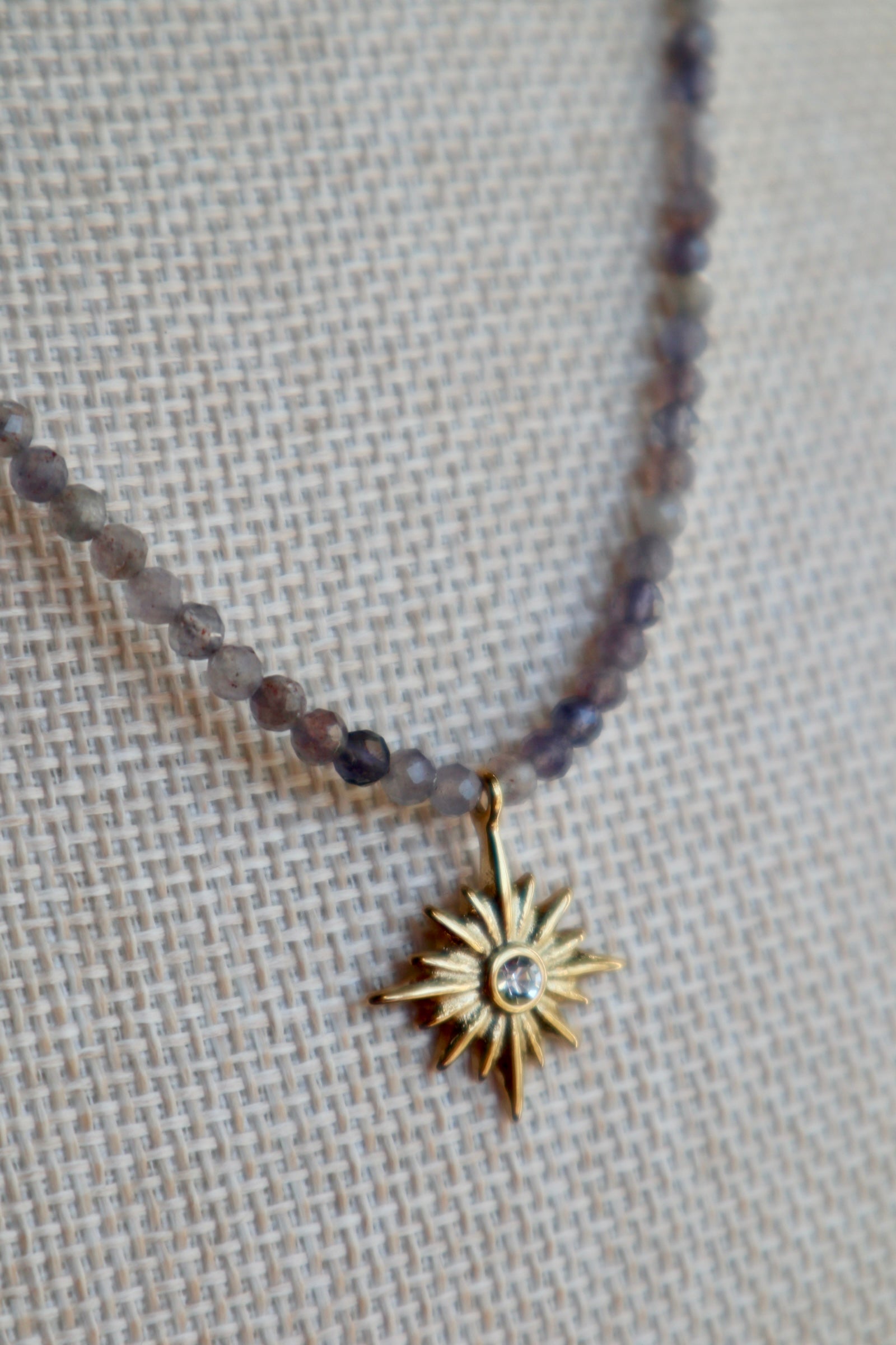 Close-up of the Astrielle necklace showing the gold radiant star pendant against deep indigo micro-faceted iolite beads