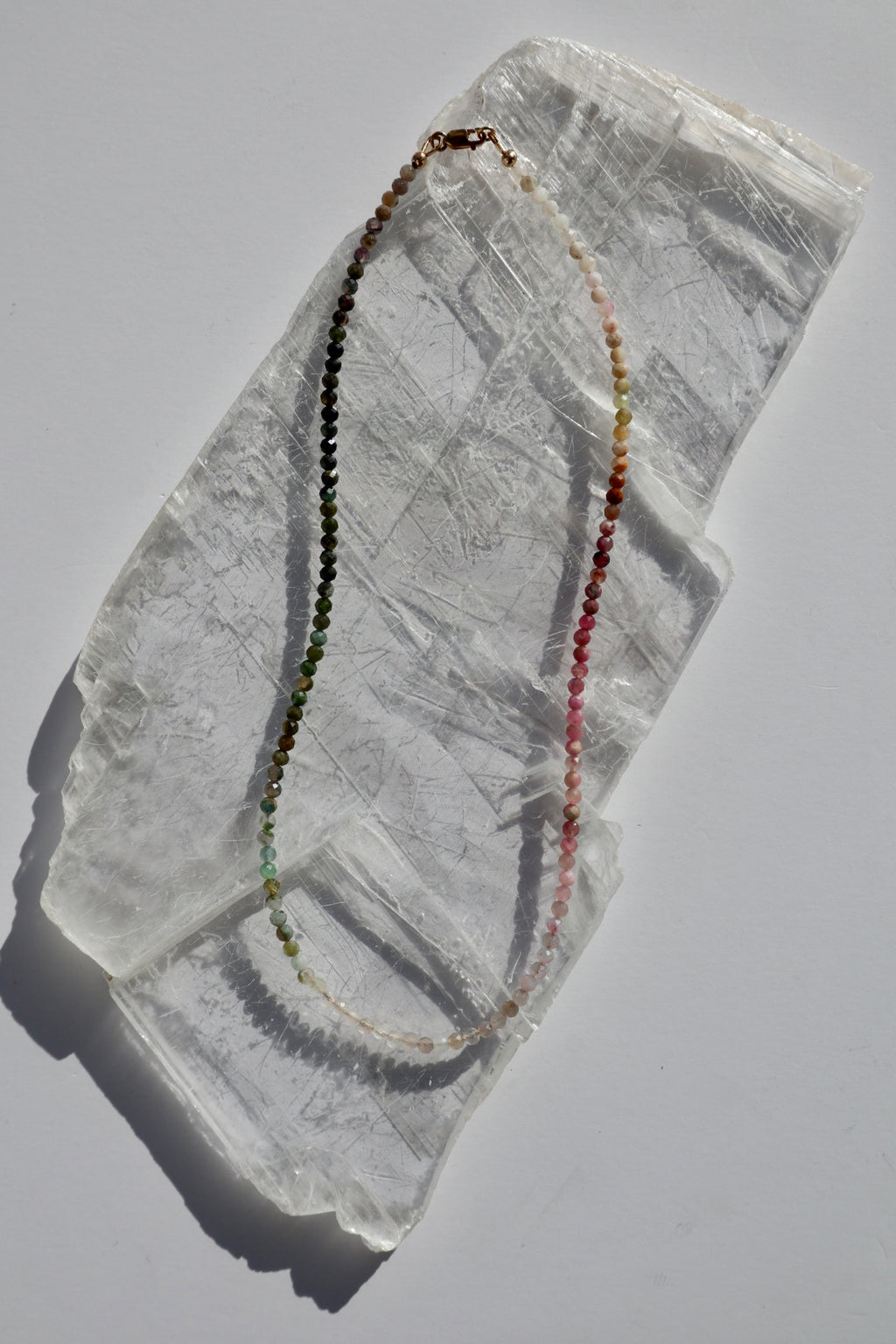 Aurora necklace by Auréad Designs, featuring multicolored micro-faceted tourmaline gemstone beads in a gradient arrangement with a 14k gold-filled lobster clasp, laid flat on a white selenite slab