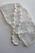 Aveline necklace by Auréad Designs, featuring mixed freshwater pearl shapes including rice and nugget pearls with a 14k gold-filled lobster clasp, laid flat on a white selenite slab