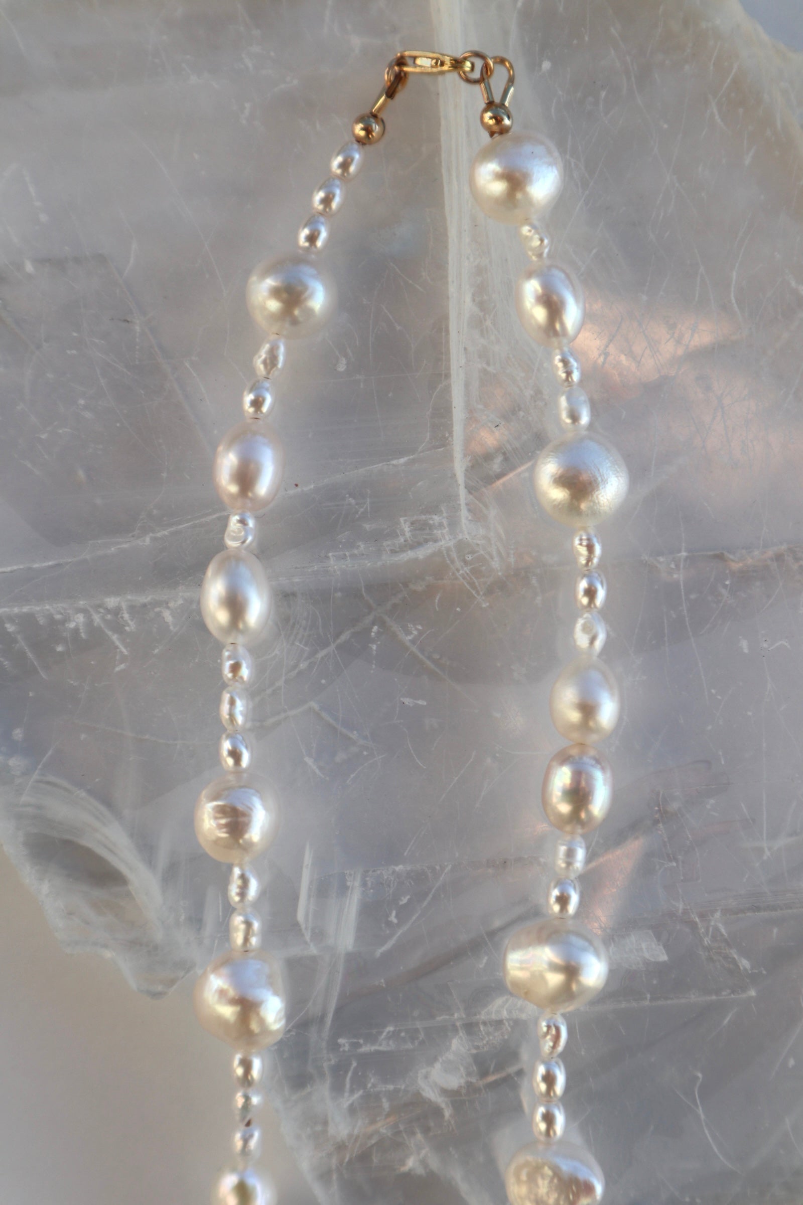 Aveline necklace by Auréad Designs draped vertically on a white selenite slab, showing the full strand of mixed freshwater rice and nugget pearls with a 14k gold-filled lobster clasp