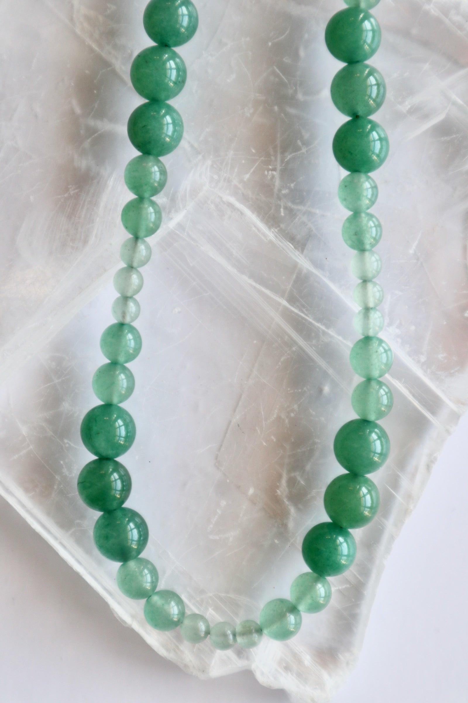 Auréad Designs Aventine green aventurine beaded necklace showing natural color variation from deep green to pale mint, flat lay on white selenite slab.