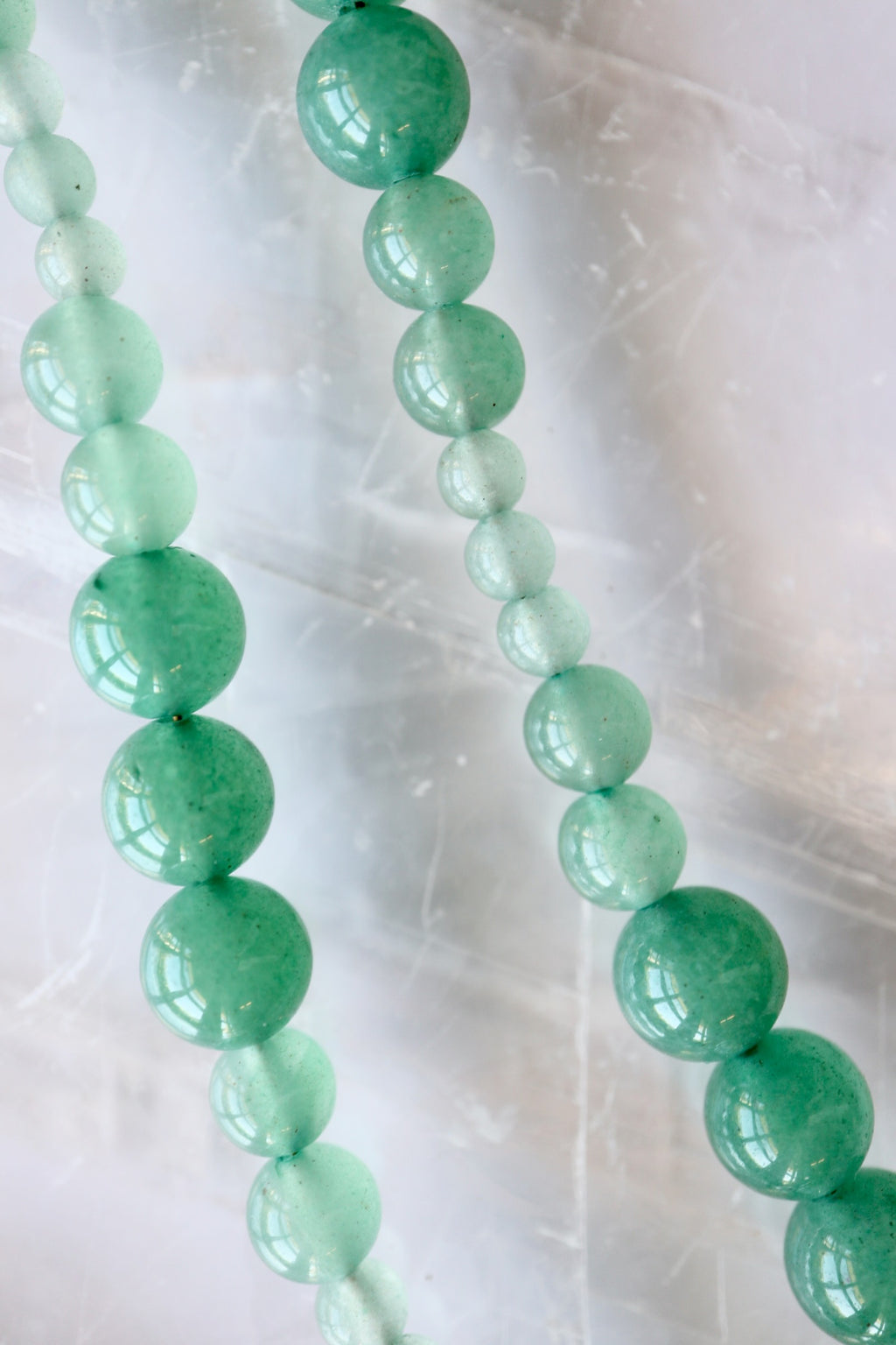 Auréad Designs Aventine green aventurine beaded necklace showing natural color variation from deep green to pale mint, flat lay on white selenite slab.