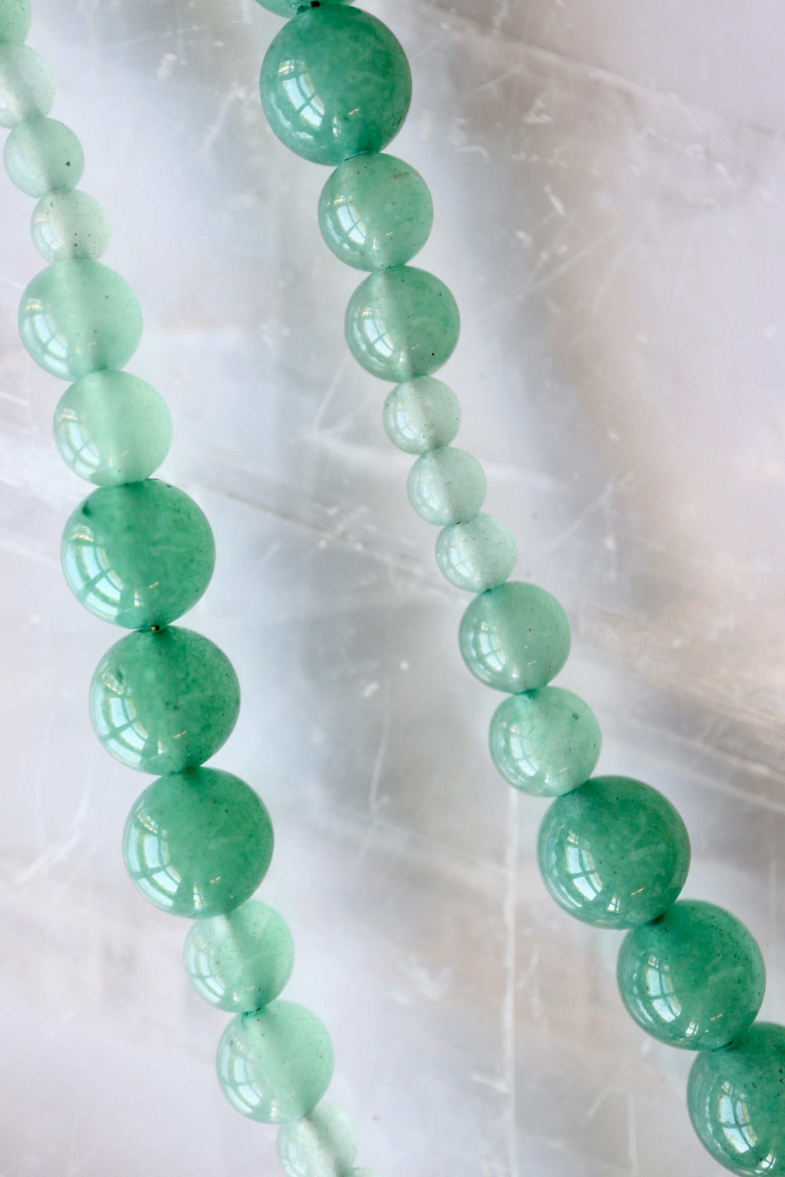 Auréad Designs Aventine green aventurine beaded necklace showing natural color variation from deep green to pale mint, flat lay on white selenite slab.