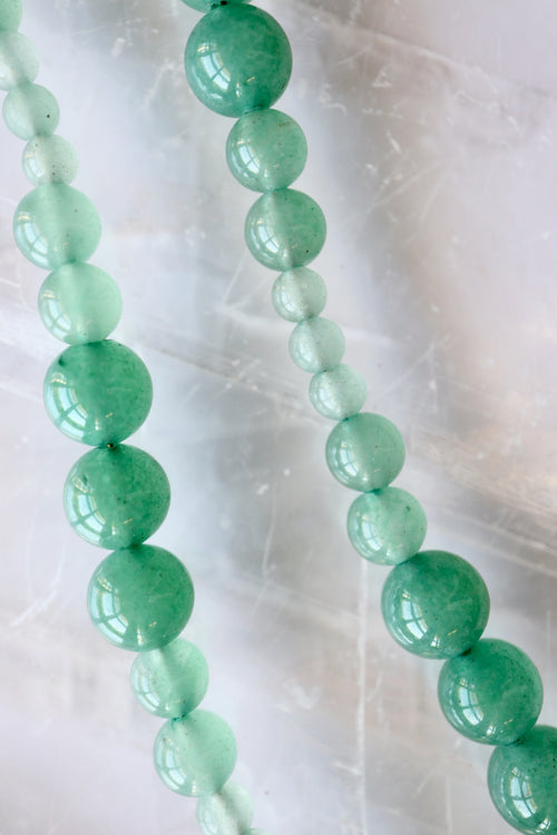 Auréad Designs Aventine green aventurine beaded necklace showing natural color variation from deep green to pale mint, flat lay on white selenite slab.