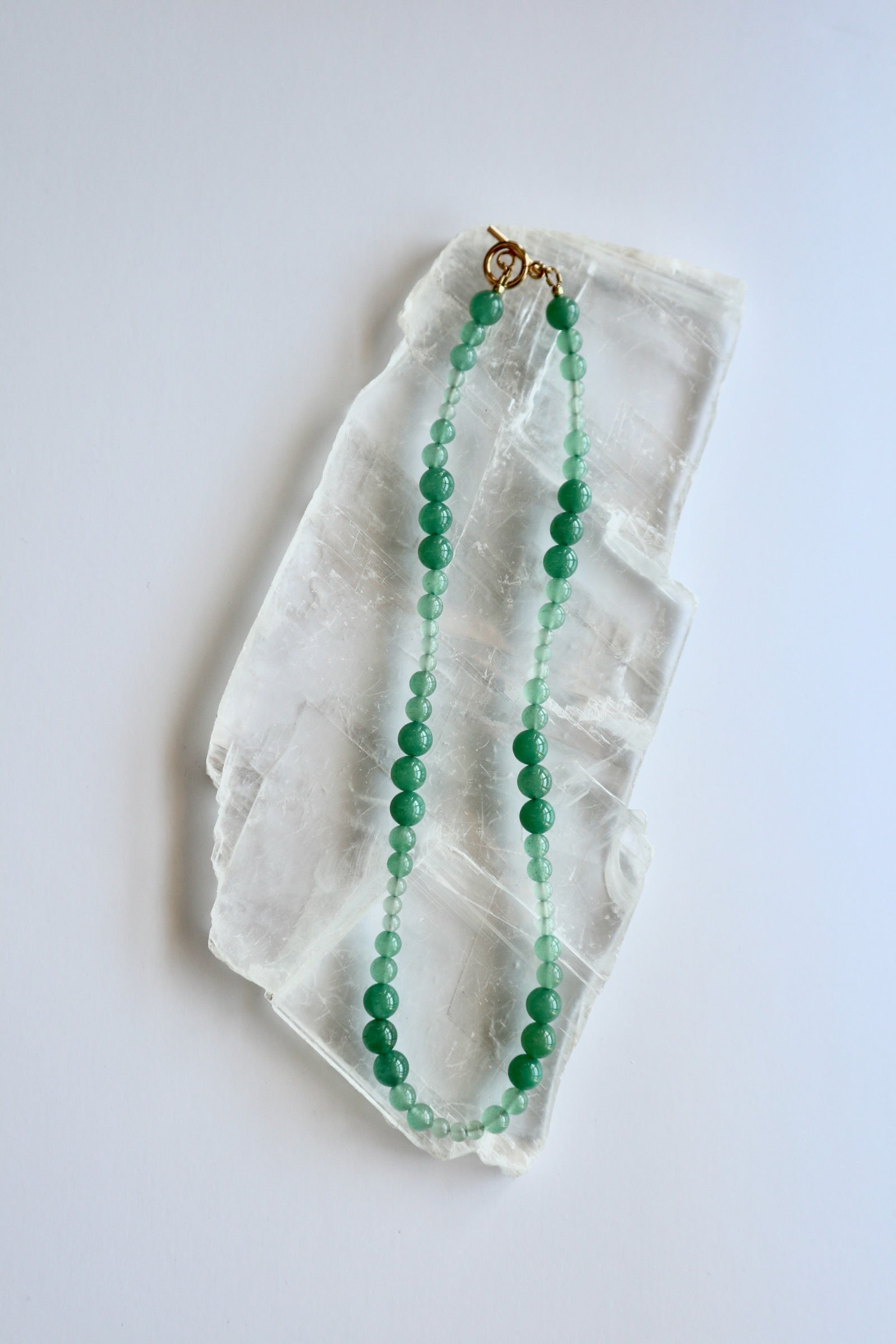 Auréad Designs Aventine green aventurine beaded necklace with gold toggle clasp, 18 inches, flat lay on white selenite slab.