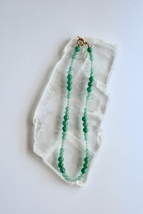 Auréad Designs Aventine green aventurine beaded necklace with gold toggle clasp, 18 inches, flat lay on white selenite slab.