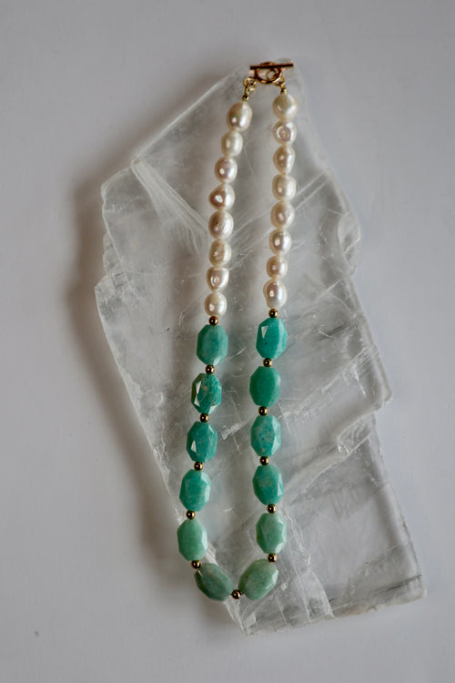 Azurea Maren amazonite and freshwater pearl necklace by Auréád Designs laid flat on a white selenite slab, showing the full strand with faceted teal amazonite stones, baroque freshwater pearls, and gold toggle clasp