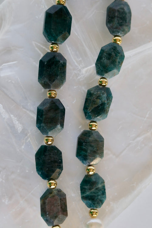 Close-up of the Azurea necklace on a white selenite slab, showing the large faceted apatite gemstone beads in deep teal-blue with their natural inclusions and gold-filled spacer beads