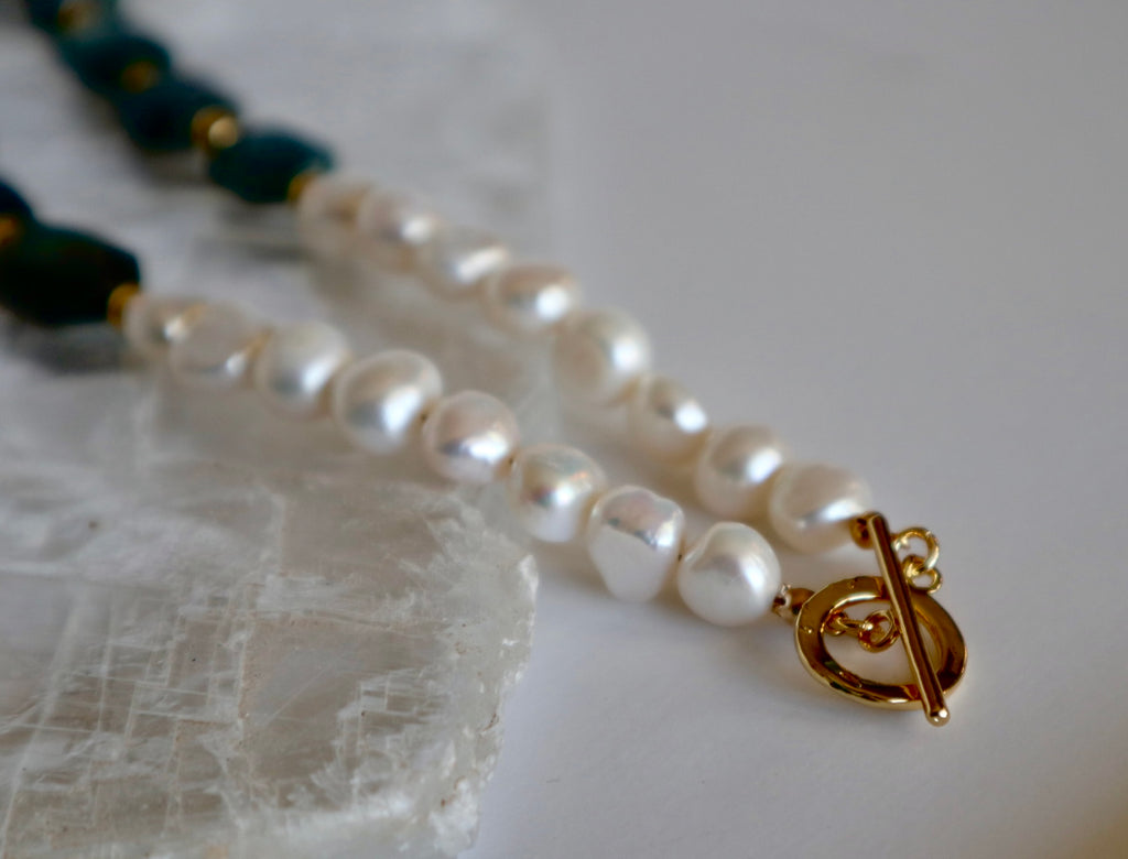 Close-up of the Azurea necklace by Auréad Designs showing freshwater pearls and a gold toggle clasp resting on a white selenite slab