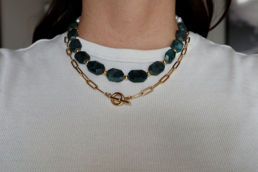 Azurea necklace by Auréad Designs featuring faceted teal gemstone beads and gold accents, worn layered with a gold paperclip chain necklace over a white top