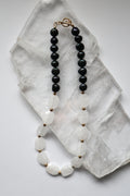 Azurea Noir necklace by Auréad Designs, featuring clear quartz beads and black pearls with gold stainless steel spacer beads and a toggle clasp, laid flat on a white selenite slab