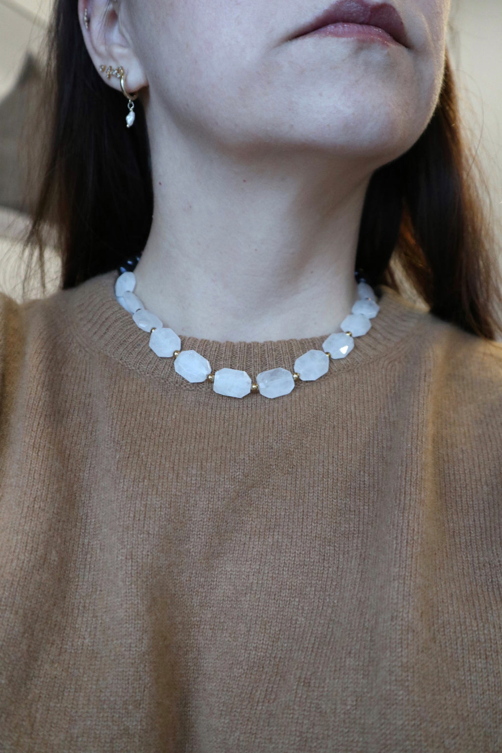 Azurea Noir necklace by Auréad Designs worn at the collarbone, styled with a camel knit sweater, showcasing the large sculptural clear quartz beads with gold spacer accents across the neckline
