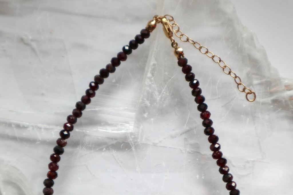 Detail shot of the Brenna necklace showing the 14k gold-filled lobster clasp and two-inch extender chain alongside the deep red faceted garnet beads