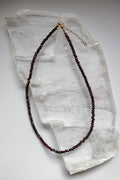 Brenna necklace by Auréad Designs, featuring faceted garnet gemstone beads with a 14k gold-filled lobster clasp and two-inch extender chain, laid flat on a white selenite slab