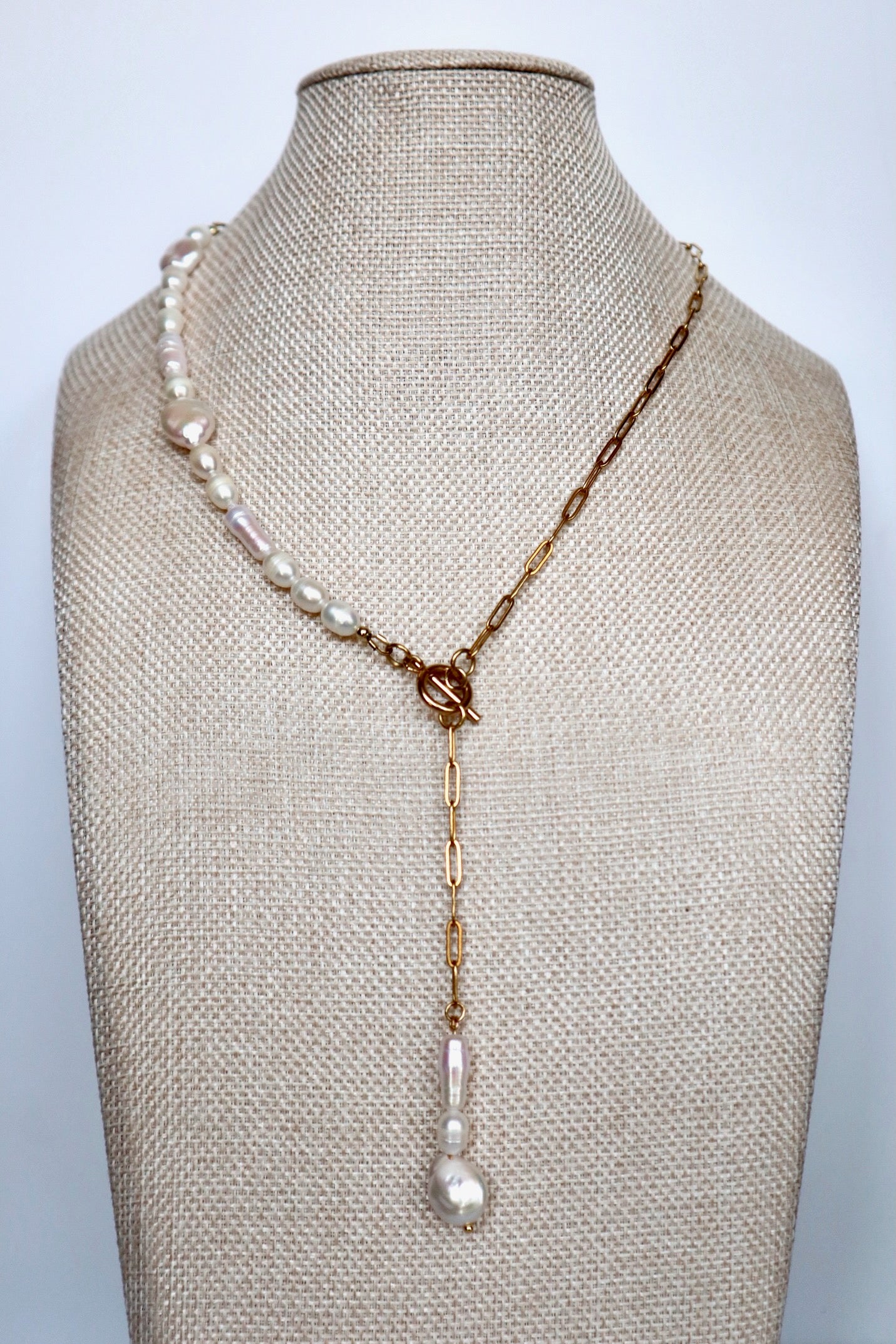 Auréad Designs Caelova lariat necklace draped at an angle on linen bust form, showing the contrast between the freshwater pearl strand half and gold paperclip chain half with pendant drop
