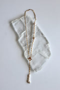 Auréad Designs Caelova lariat necklace laid flat on white selenite slab, showing gold stainless steel paperclip chain, front toggle clasp, and triple freshwater pearl pendant with baroque keshi, flat round, and rice pearls