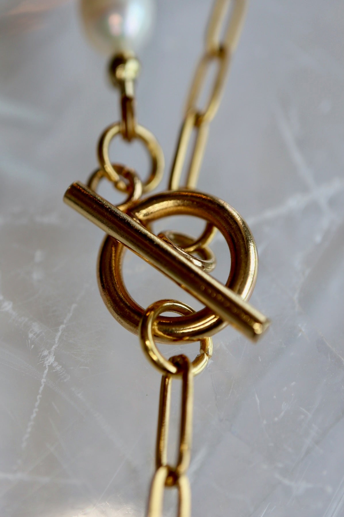Auréad Designs Caelova lariat necklace close-up of gold stainless steel toggle clasp and paperclip chain links on white selenite slab