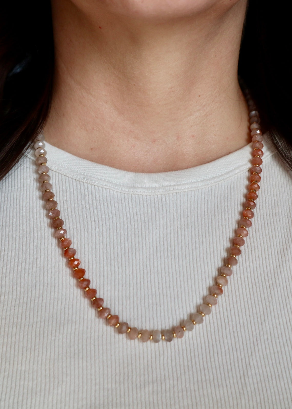 Calida peach moonstone and freshwater pearl necklace worn at the collarbone, showing the warm radiant glow of the moonstone beads and the gentle contrast of the pearls against skin