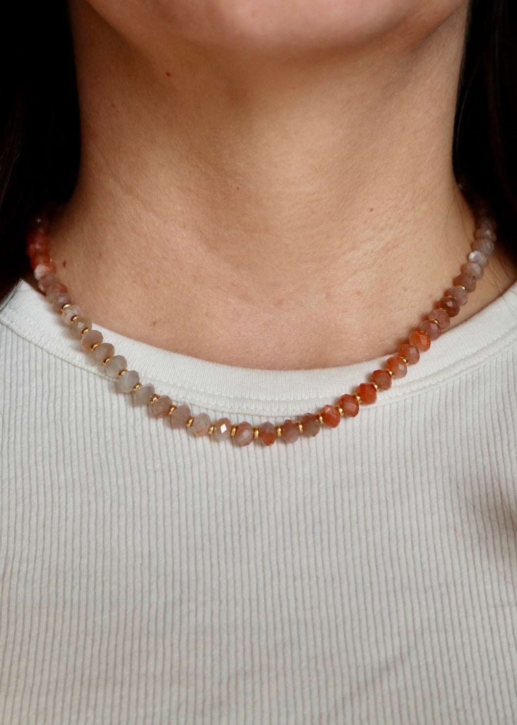 Close-up of the Calida necklace resting at the collarbone, highlighting the warm luminous tones of peach moonstone beads and the soft contrast of freshwater pearls with gold spacer accents