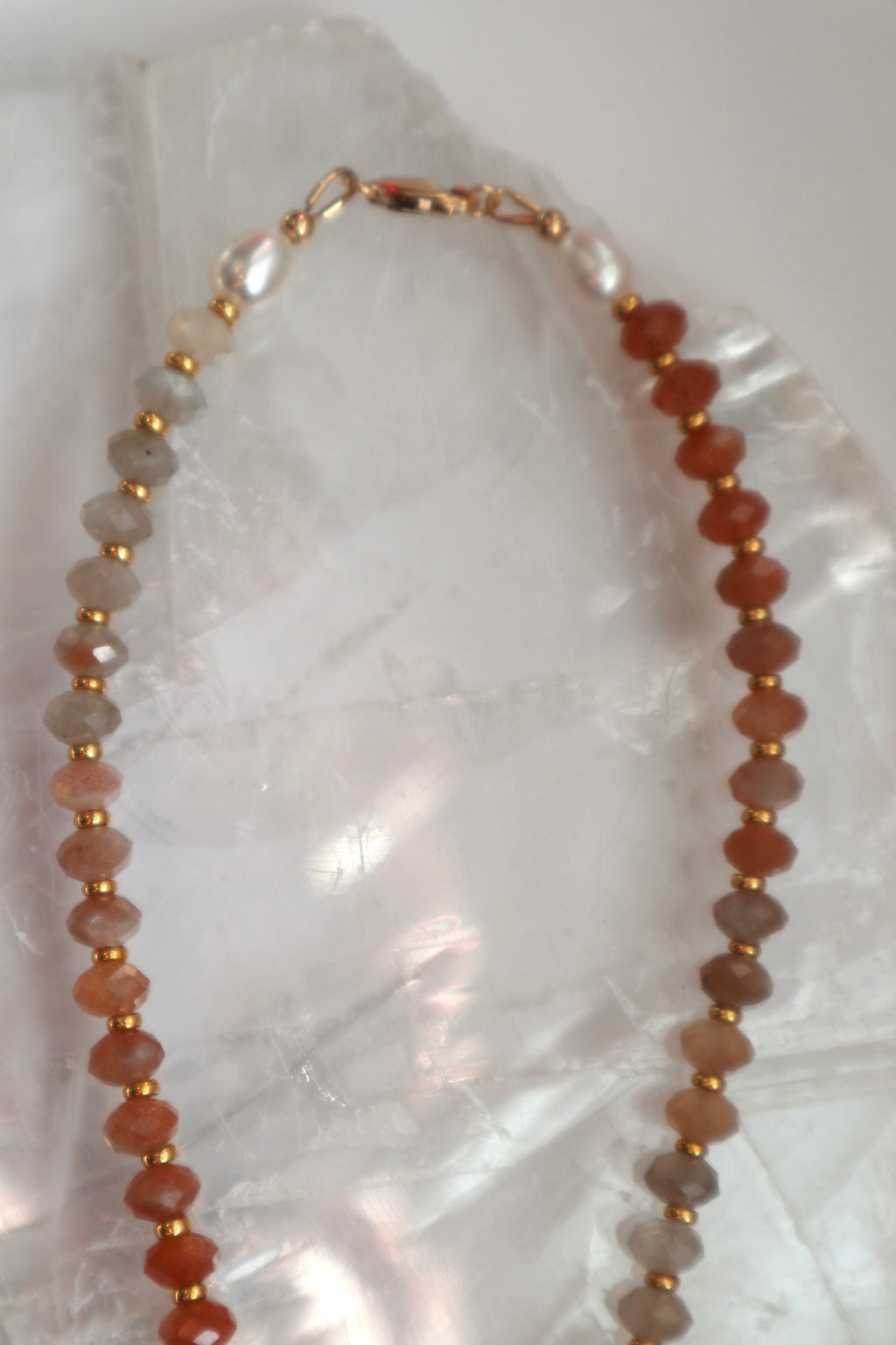 Detail shot of the Calida necklace highlighting the 14k gold-filled clasp and the natural peach tones and soft glow of the moonstone beads alongside freshwater pearls