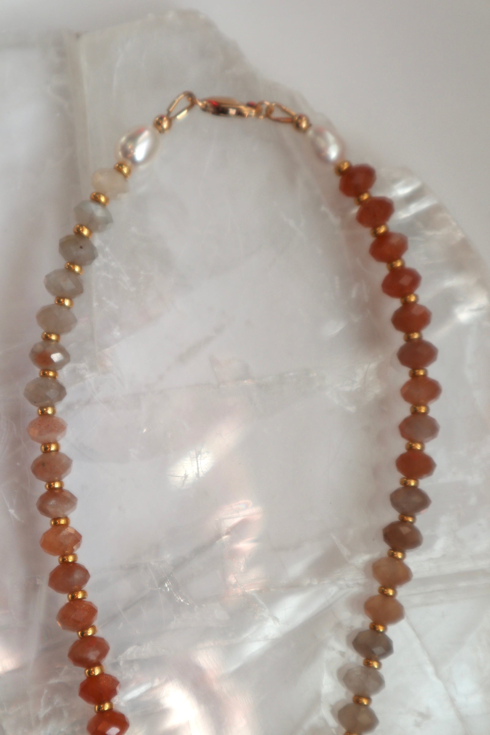 Detail shot of the Calida necklace highlighting the 14k gold-filled clasp and the natural peach tones and soft glow of the moonstone beads alongside freshwater pearls