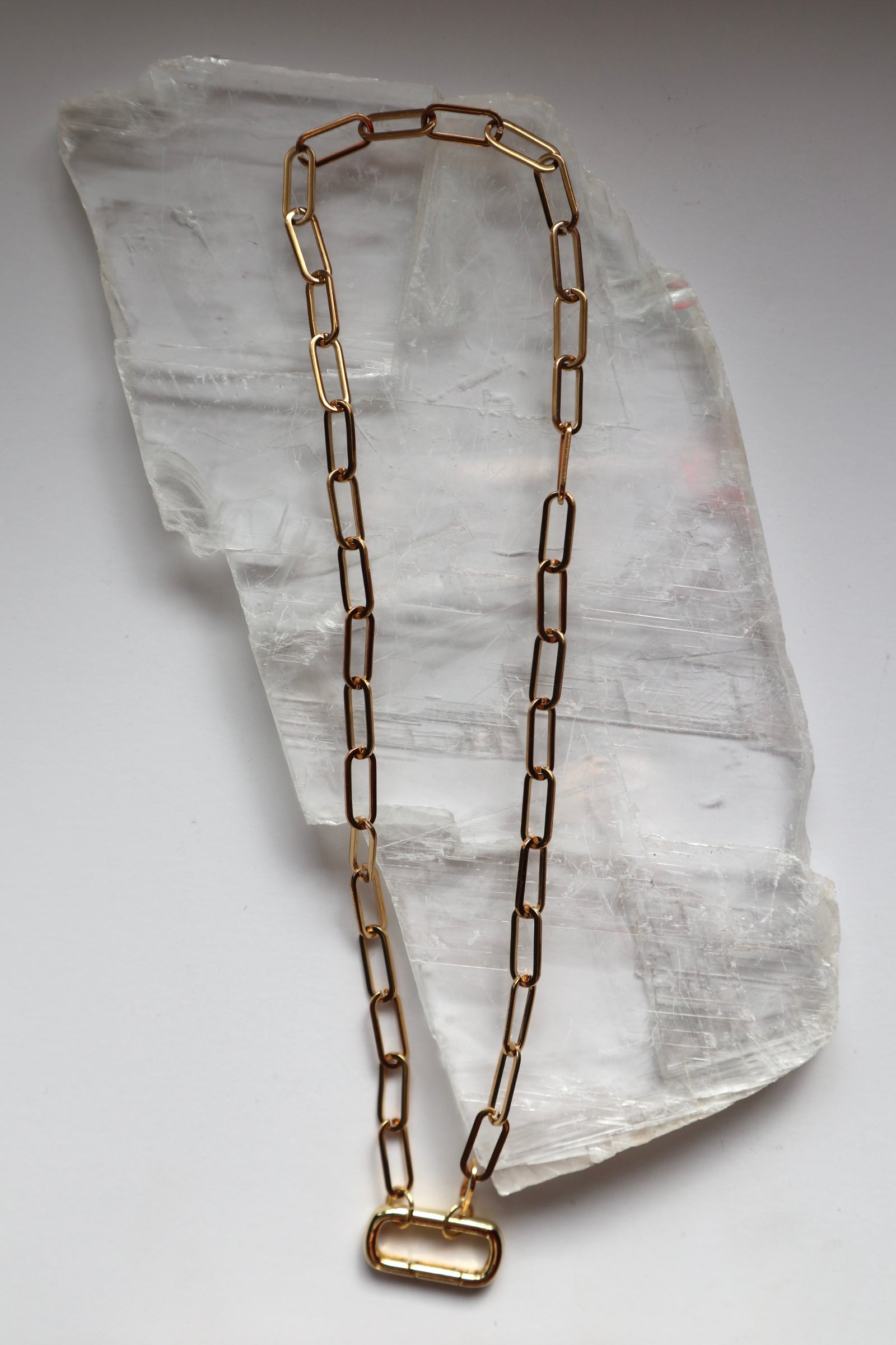 Catenne necklace by Auréad Designs laid flat on a white selenite slab, showing the full length of the 18k gold PVD stainless steel paperclip chain with the carabiner clasp as a focal point at the base