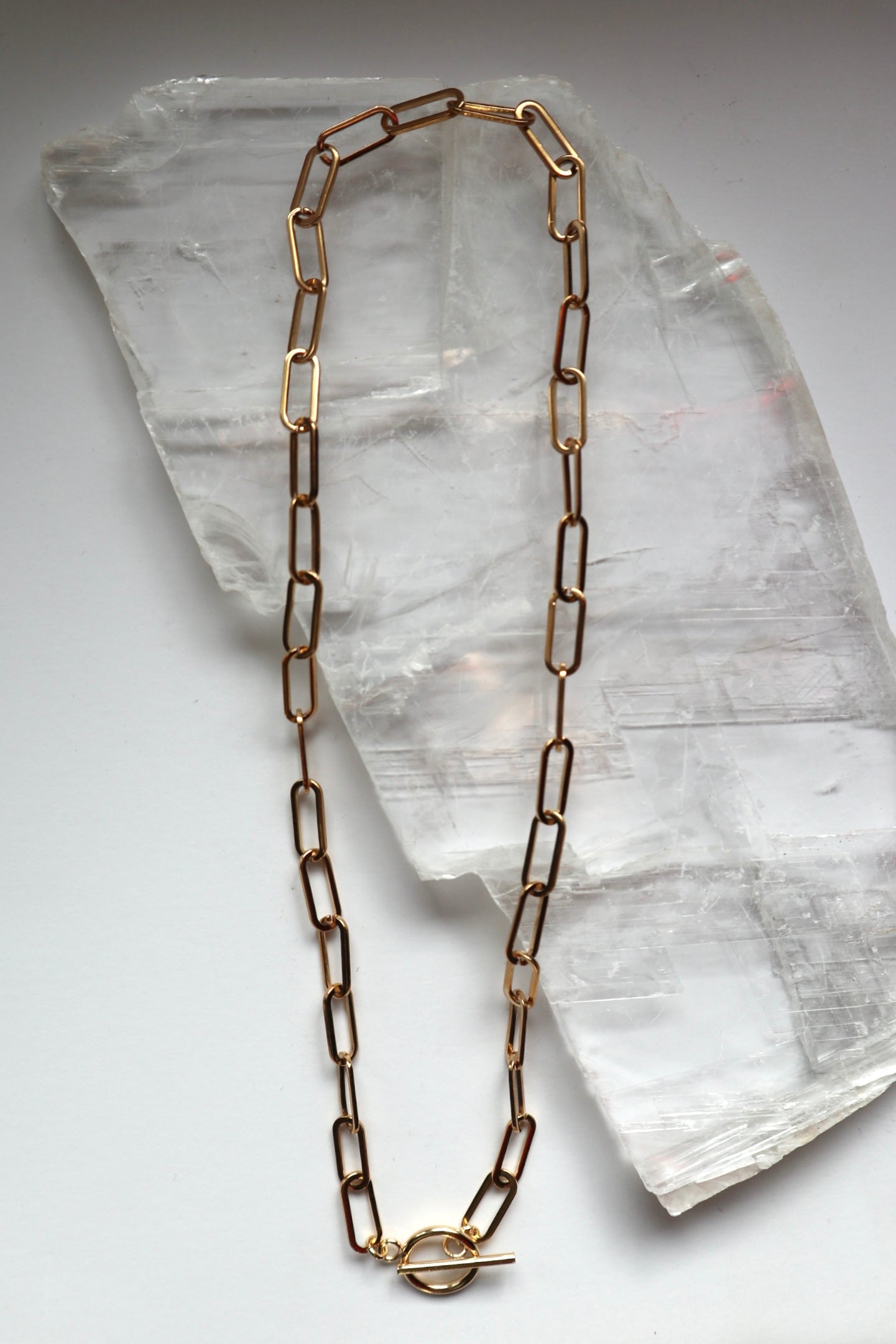 Catenne necklace by Auréad Designs, featuring an 18k gold PVD stainless steel paperclip chain with a toggle clasp, laid flat on a white selenite slab