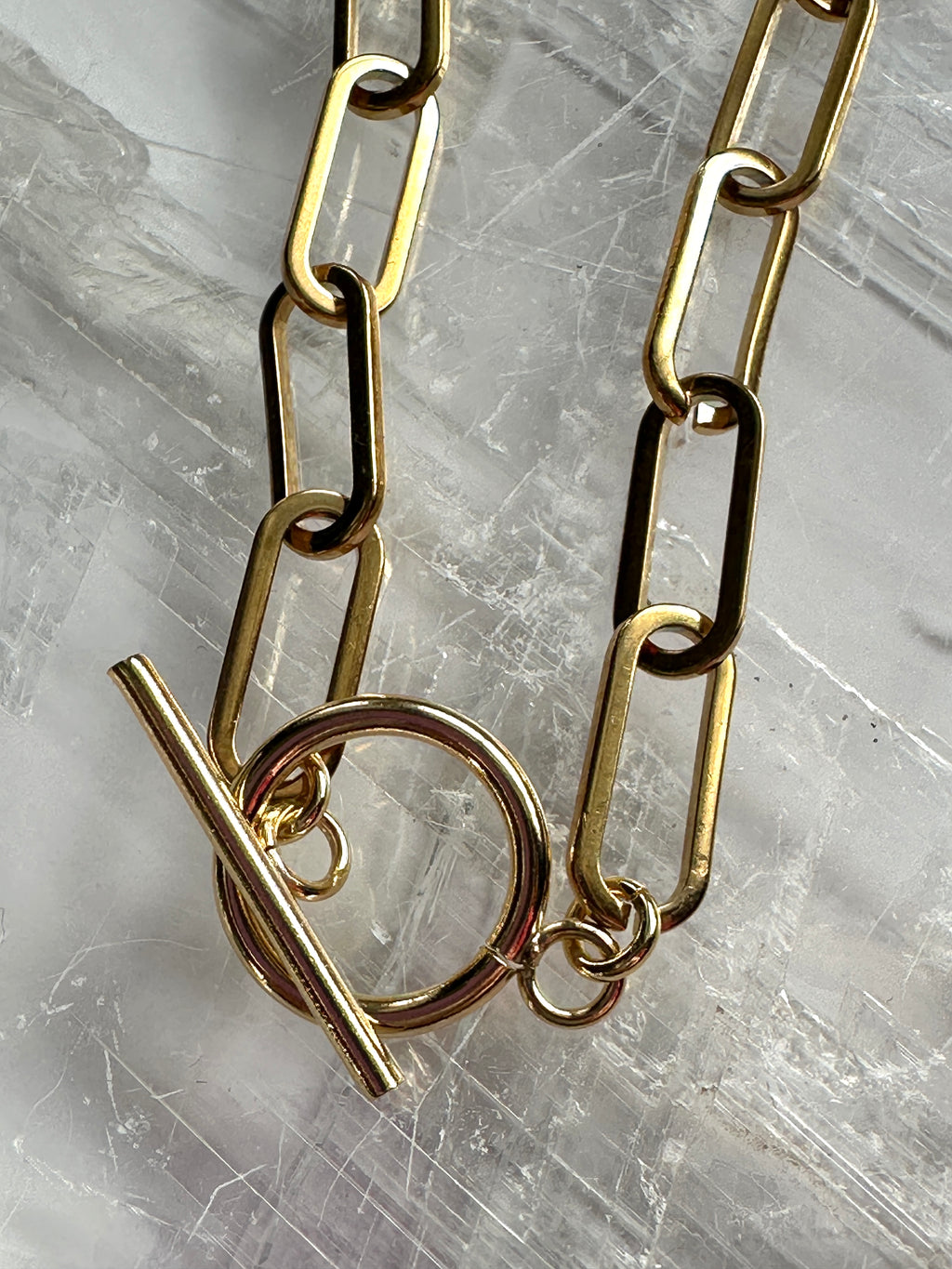 Close-up of the Catenne necklace showing the elongated 18k gold PVD stainless steel paperclip chain links and toggle clasp