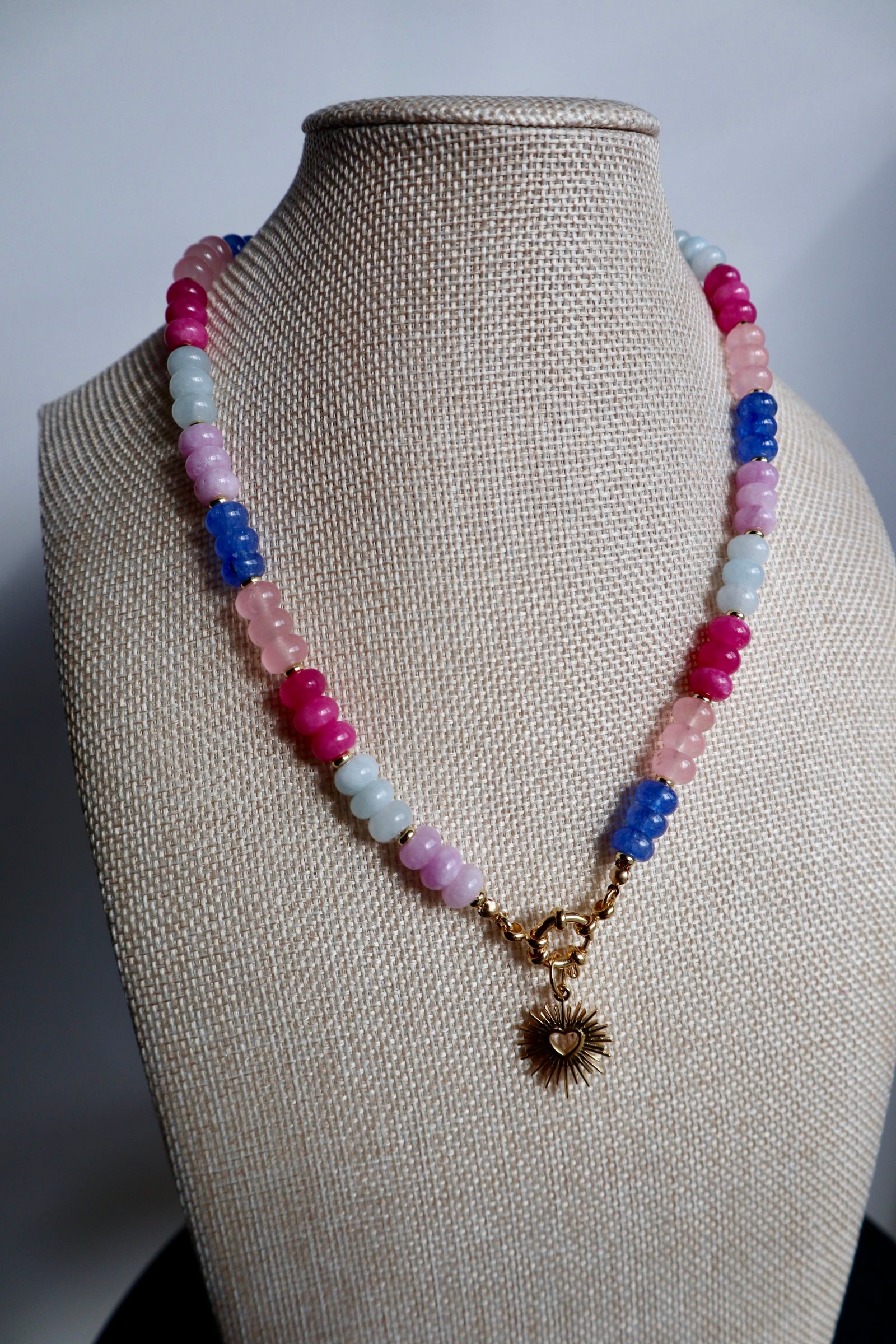 Cherise necklace by Auréad Designs on linen bust, showing the full strand of pink and purple jade rondelle beads with the gold radiant heart pendant as a focal point