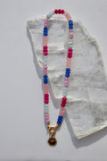 Cherise necklace by Auréad Designs, featuring dyed pink and purple jade rondelle beads and a gold stainless steel radiant heart pendant with a sailor spring clasp, laid flat on a white selenite slab
