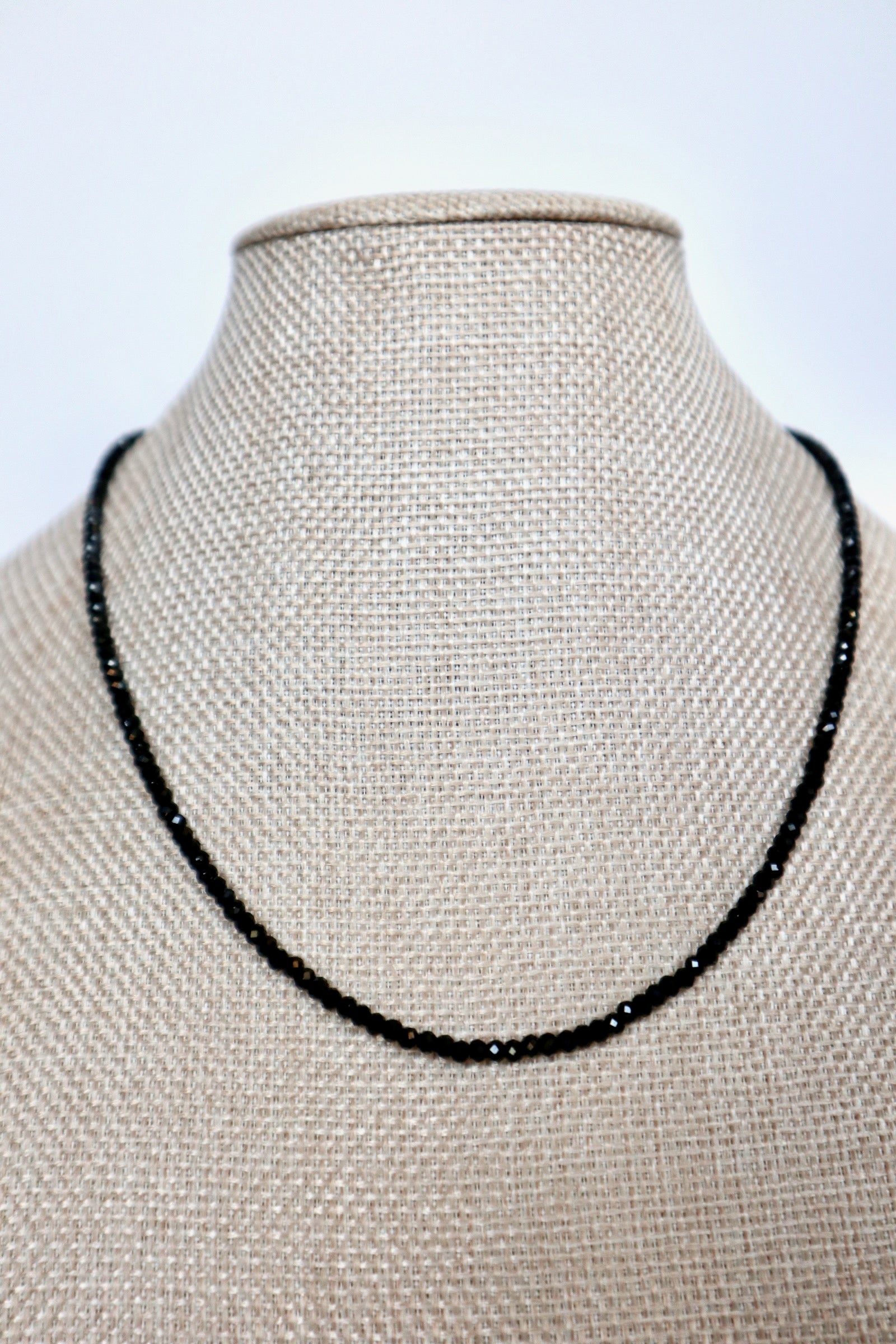Auréad Designs Corvine necklace displayed front-facing on linen bust form, continuous strand of faceted black spinel beads sitting at collarbone length