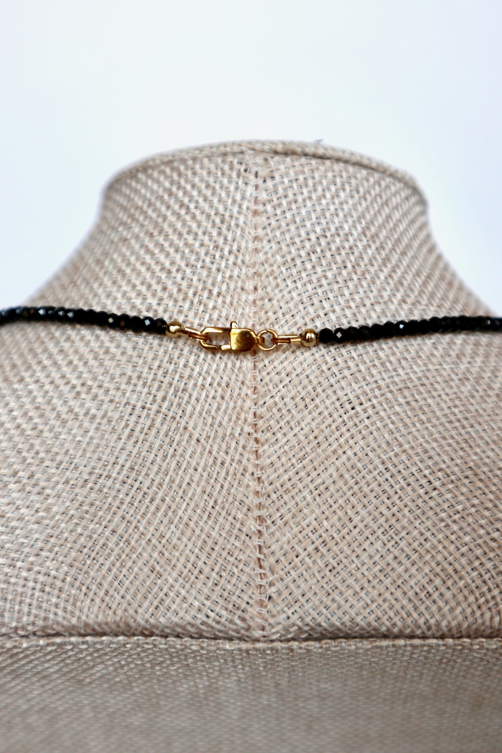 Auréad Designs Corvine necklace back clasp detail showing gold stainless steel lobster claw clasp with black spinel bead strand on linen bust form