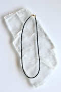 Auréad Designs Corvine necklace laid flat on white selenite slab, showing full strand of 3x2mm faceted rondelle black spinel beads with gold stainless steel lobster clasp