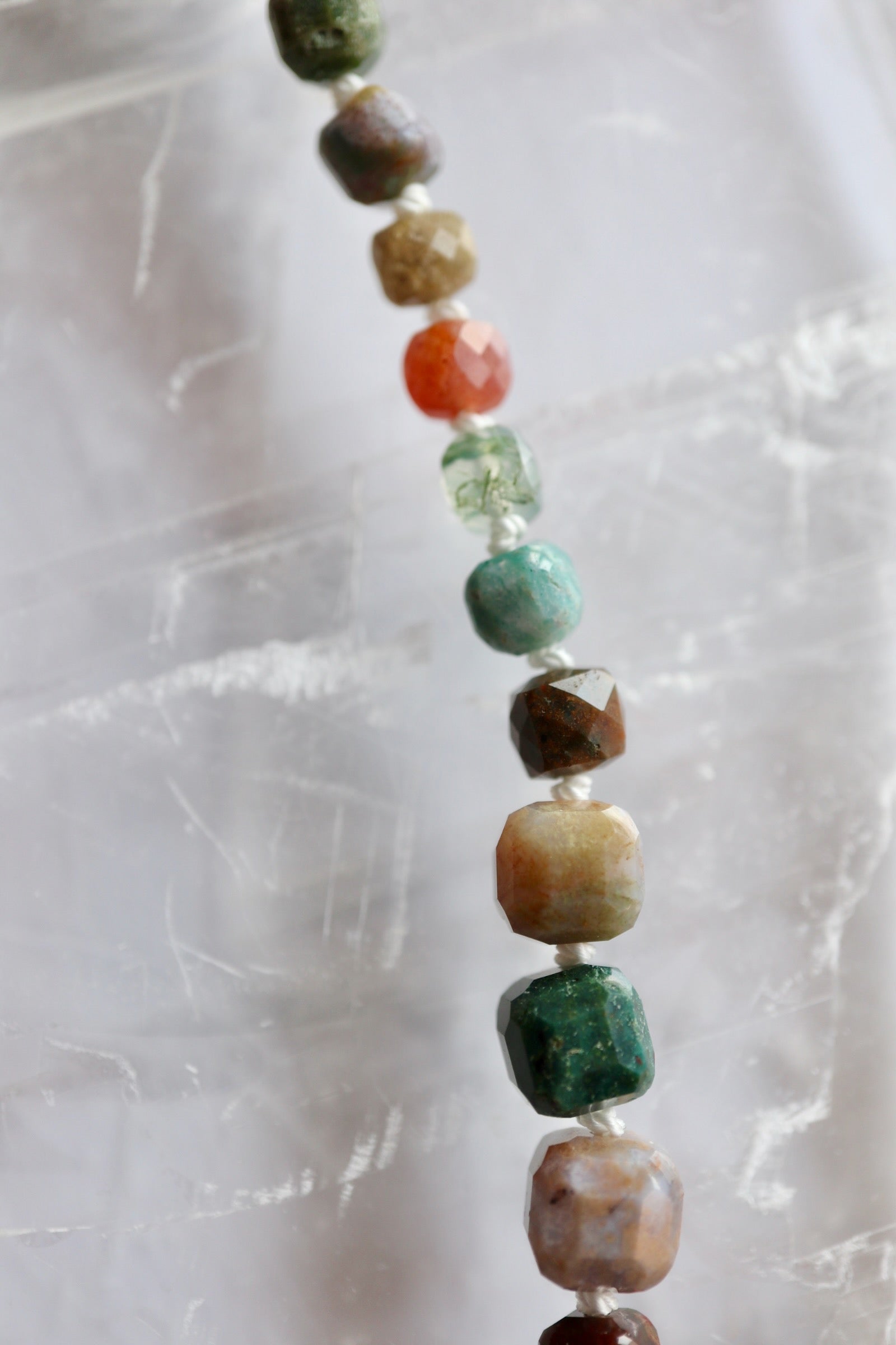 Close-up of faceted indian agate cube beads on the Current necklace by Auréad Designs, showing individual color variation in orange, teal, moss green, and amber tones against a white selenite background