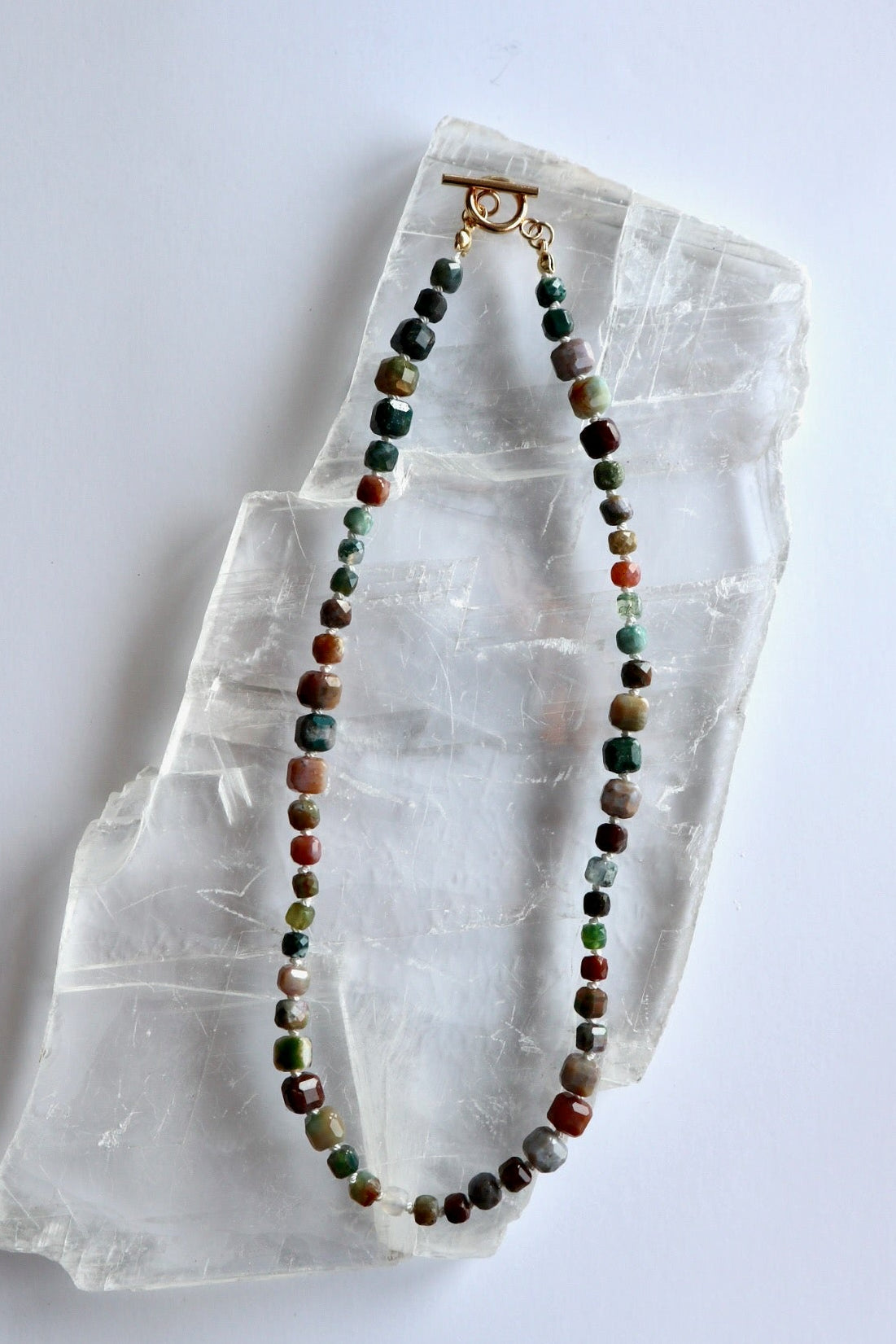 Current necklace by Auréad Designs laid in a circle on a white selenite crystal, showing the full strand of multicolored indian agate beads from the Glacier Collection