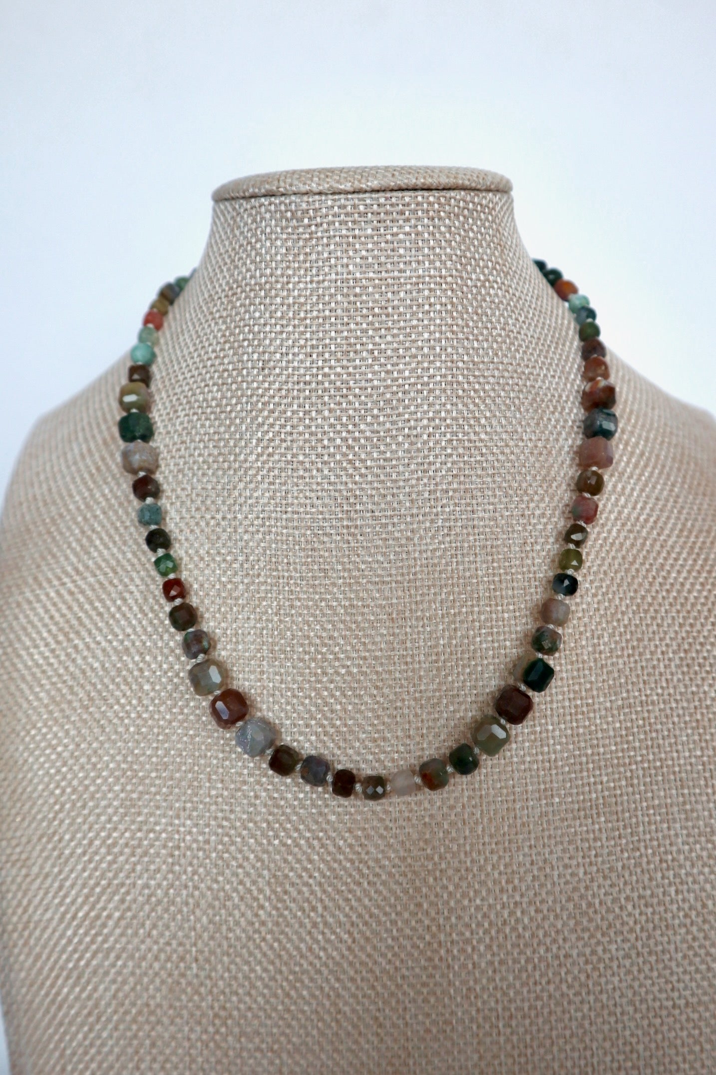 Current necklace by Auréad Designs displayed on a linen bust, front view of the full silk-knotted indian agate strand in natural red, green, brown, and teal tones, from the Glacier Collection