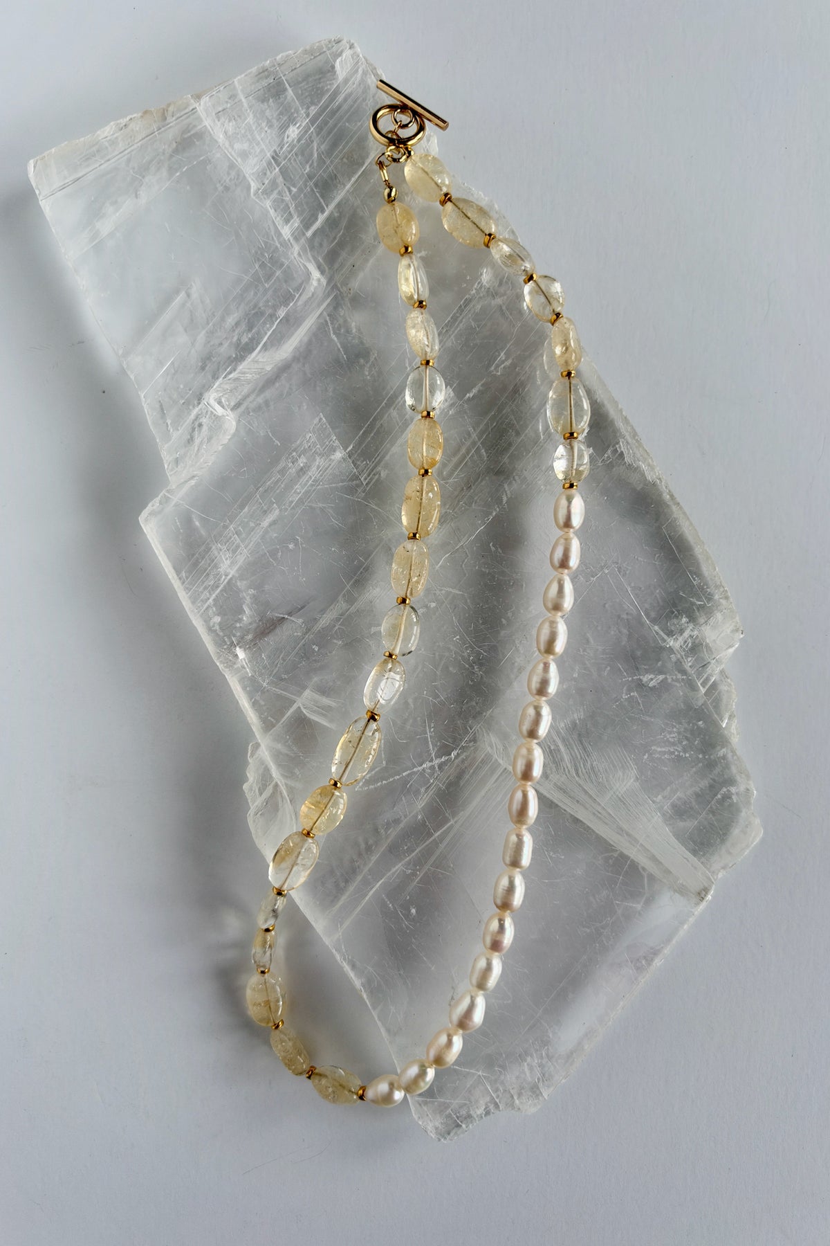 Dawn citrine and freshwater pearl necklace by Auréad Designs on white selenite slab, full length flat lay