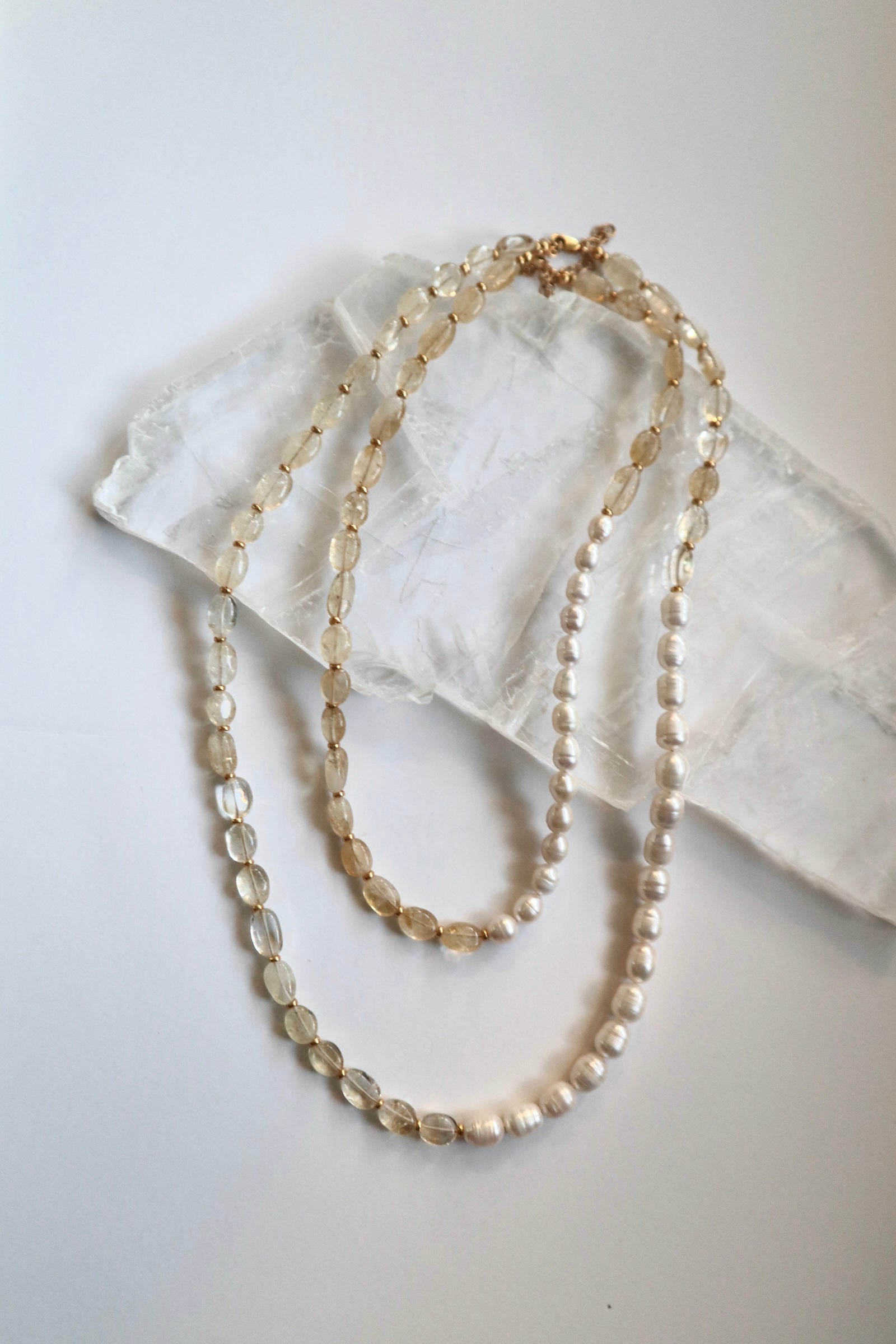 Dawn necklace by Auréad Designs in both available lengths draped on a white selenite slab, showing the asymmetrical citrine gemstone bead and freshwater pearl design side by side