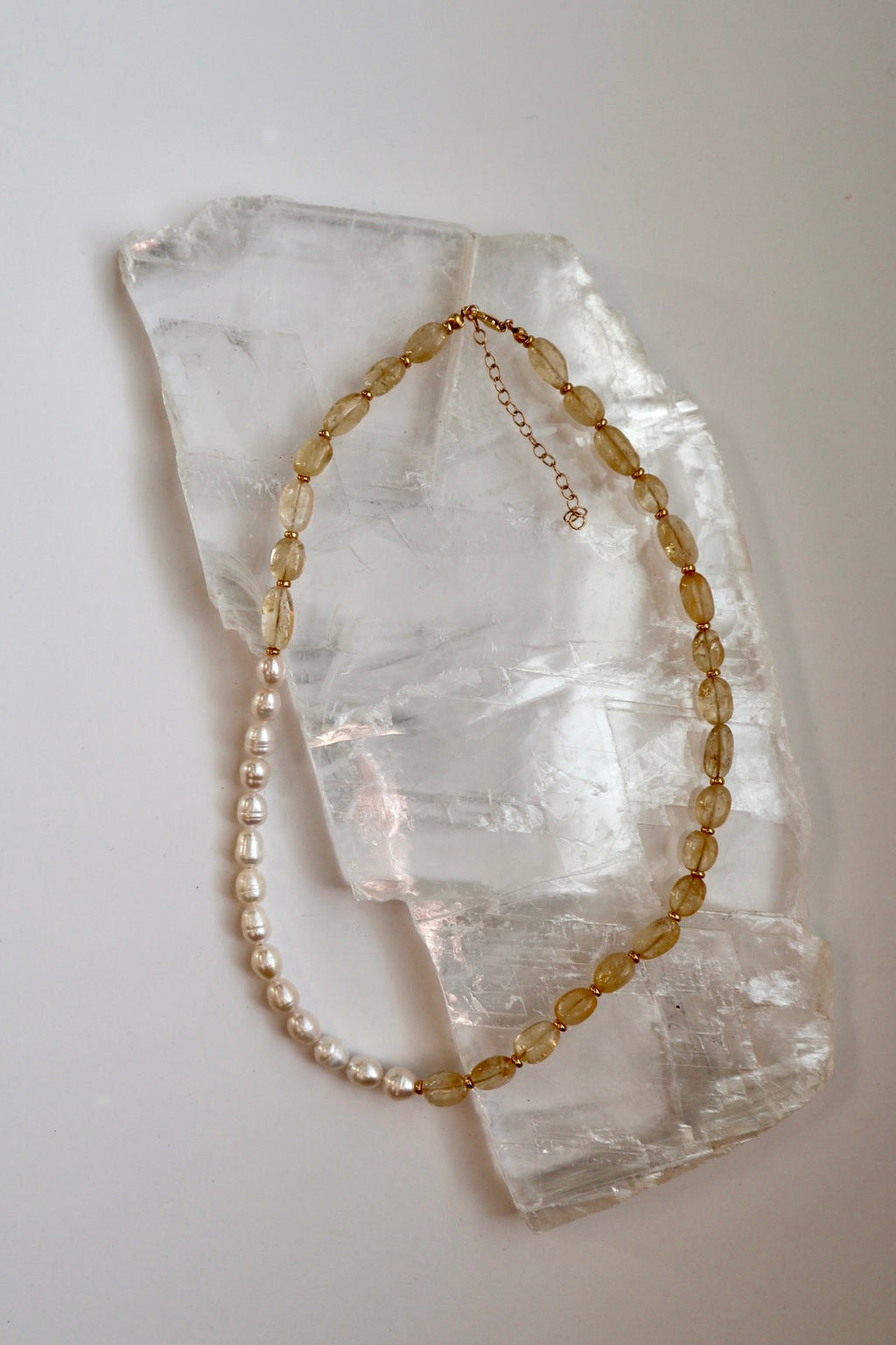 Dawn necklace by Auréad Designs, featuring citrine gemstone beads and freshwater pearls with galvanized gold spacer beads and a 14k gold-filled clasp, laid flat on a white selenite slab