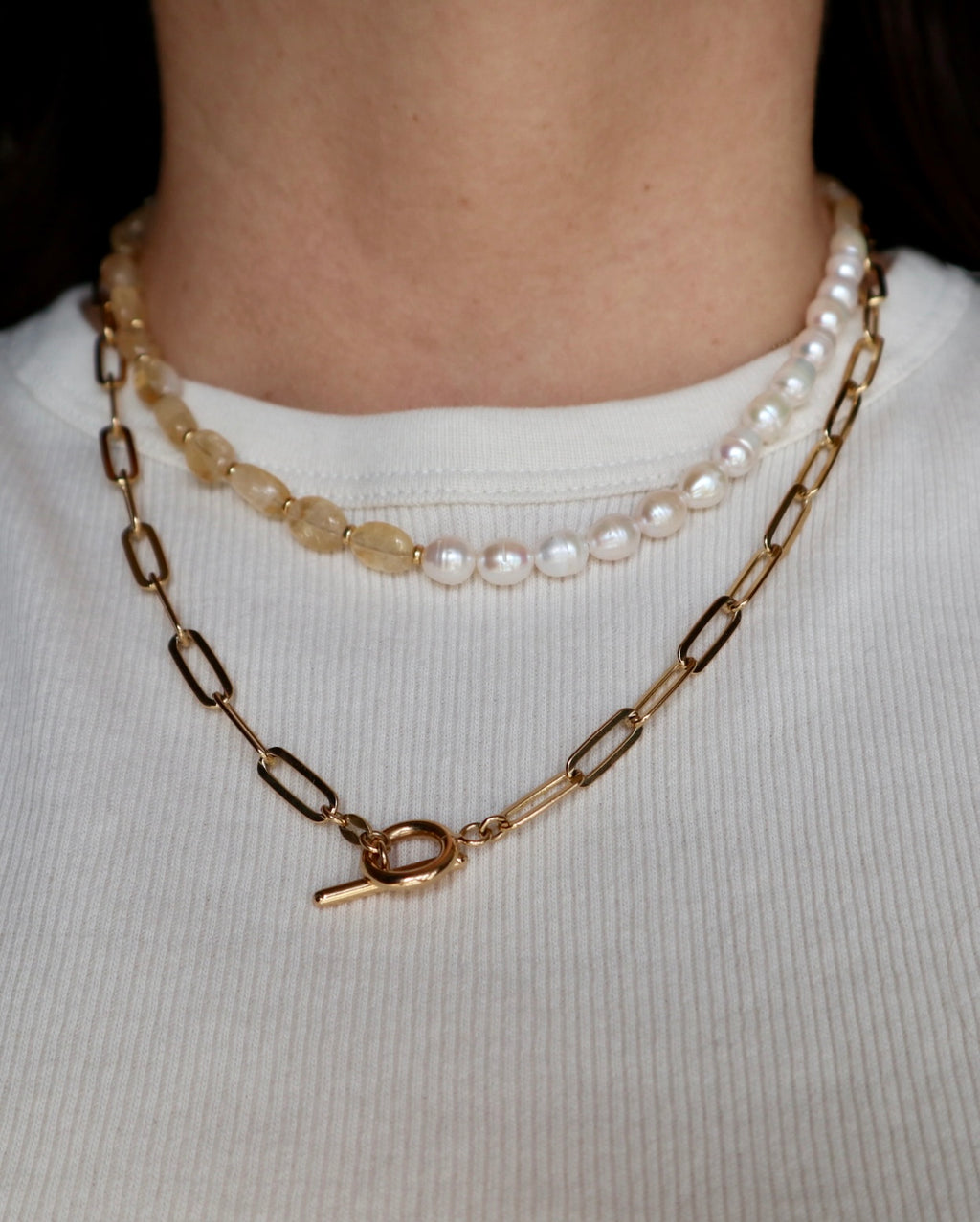 Dawn necklace by Auréad Designs layered on model with a freshwater pearl necklace and a gold paperclip chain, styled with a white ribbed top to show a curated necklace stack