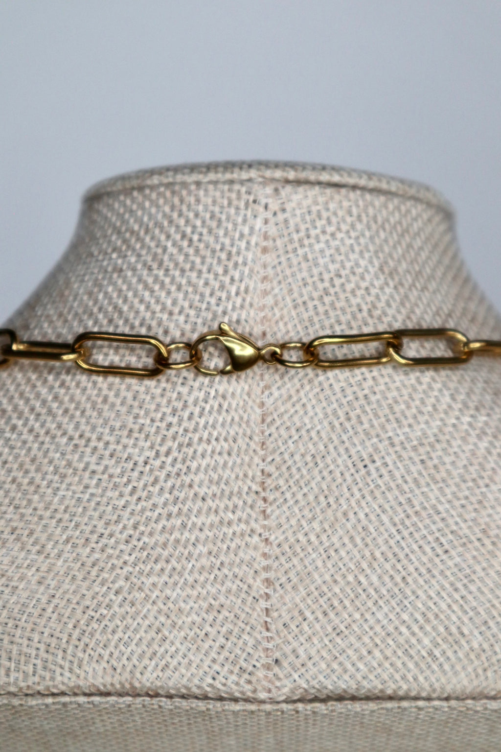 Close-up of the lobster claw clasp on the Elavene gold paperclip chain necklace by Auréád Designs, displayed on a linen bust form